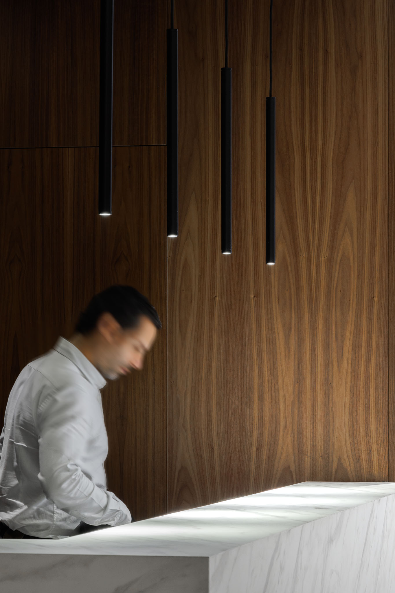 Recepção: Detalhe do balcão em mármore branco e parede em madeira com candeeiros suspensos. — Clínica de fisioterapia - Fisiminho arquitetura L2C Arquitetura em Braga