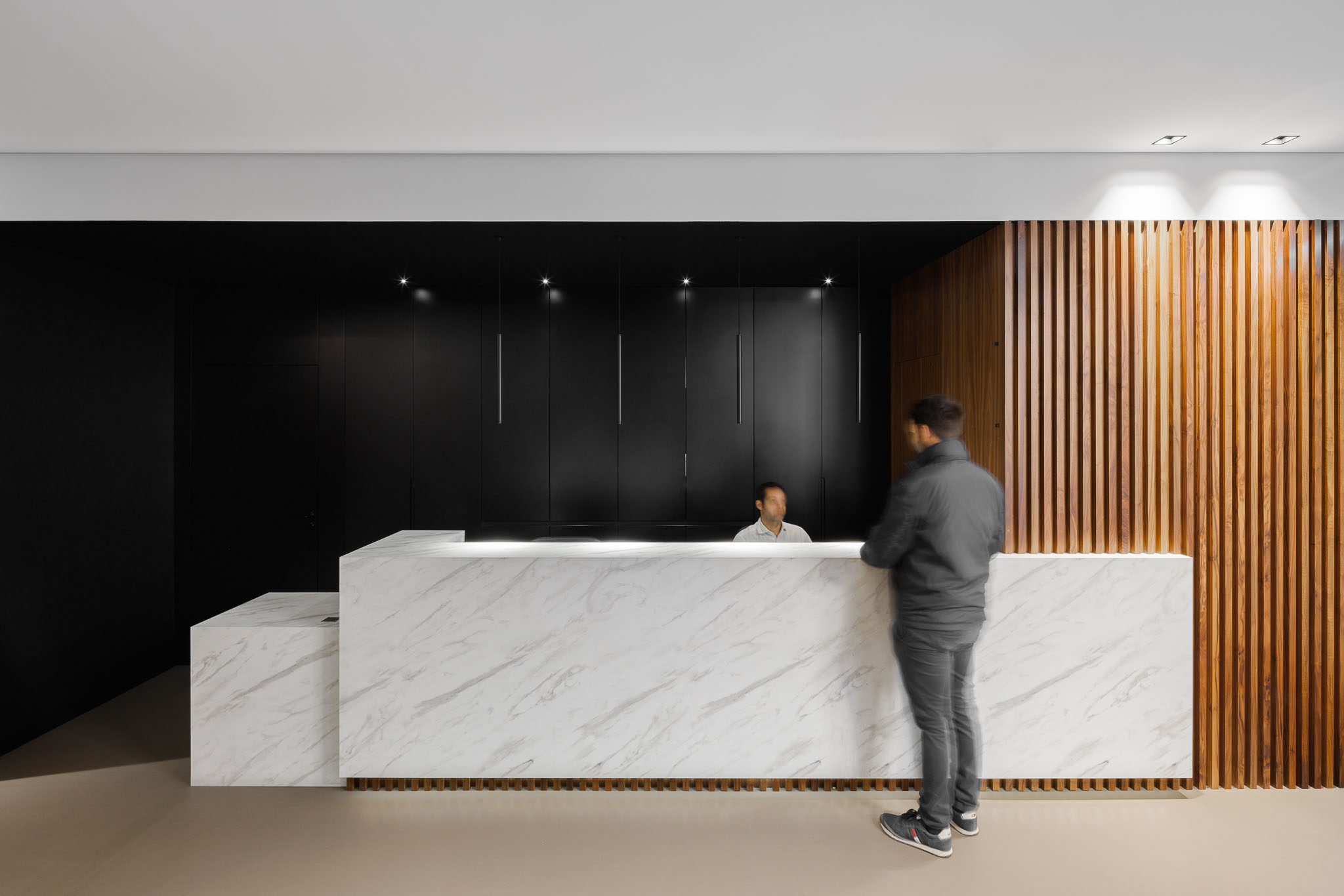 Recepção: Balcão em mármore branco com parede preta e revestimento em madeira vertical. — Clínica de fisioterapia - Fisiminho arquitetura L2C Arquitetura em Braga