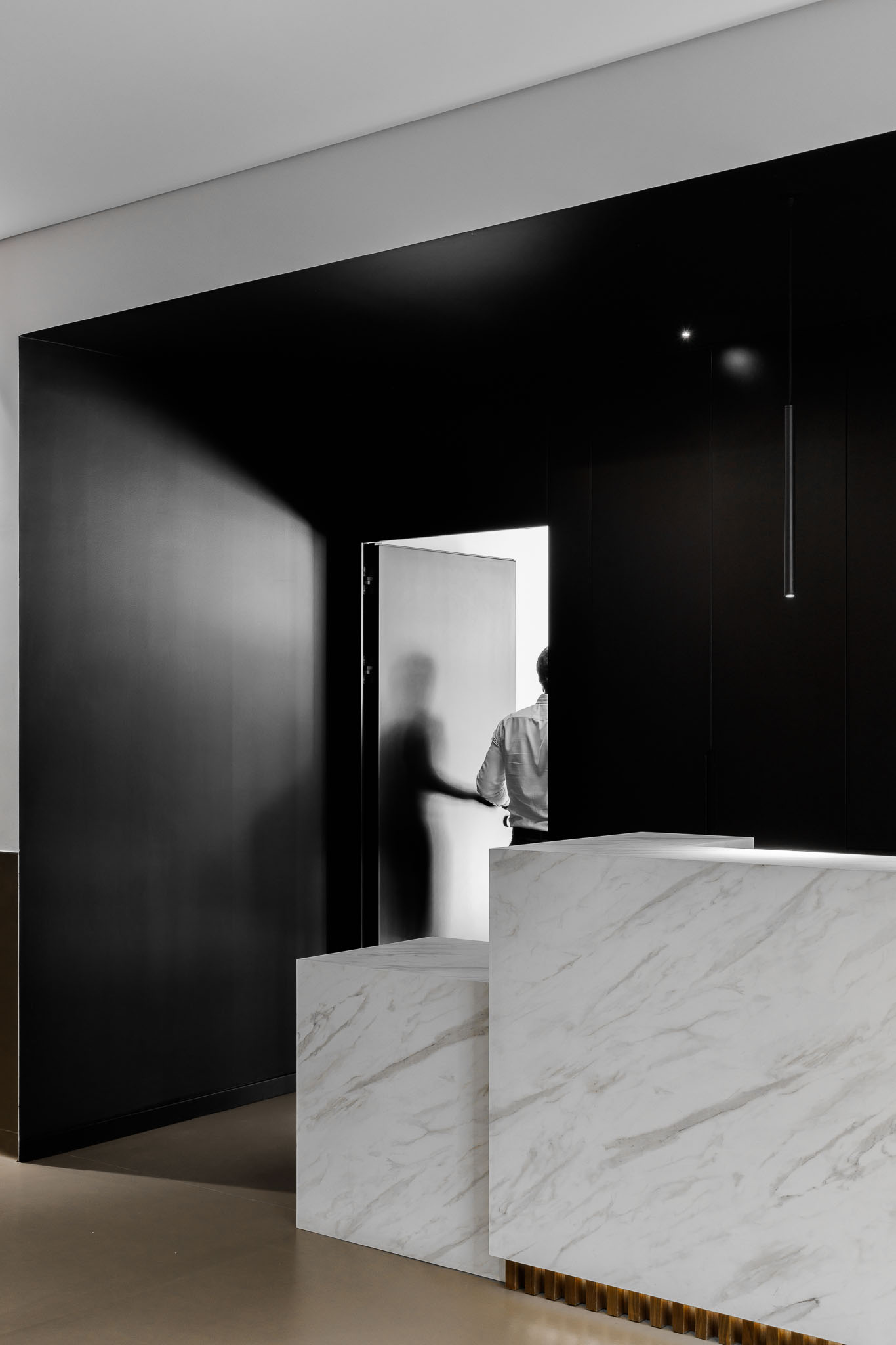 Recepção: Balcão em mármore branco com parede preta e porta envidraçada ao fundo. — Clínica de fisioterapia - Fisiminho arquitetura L2C Arquitetura em Braga