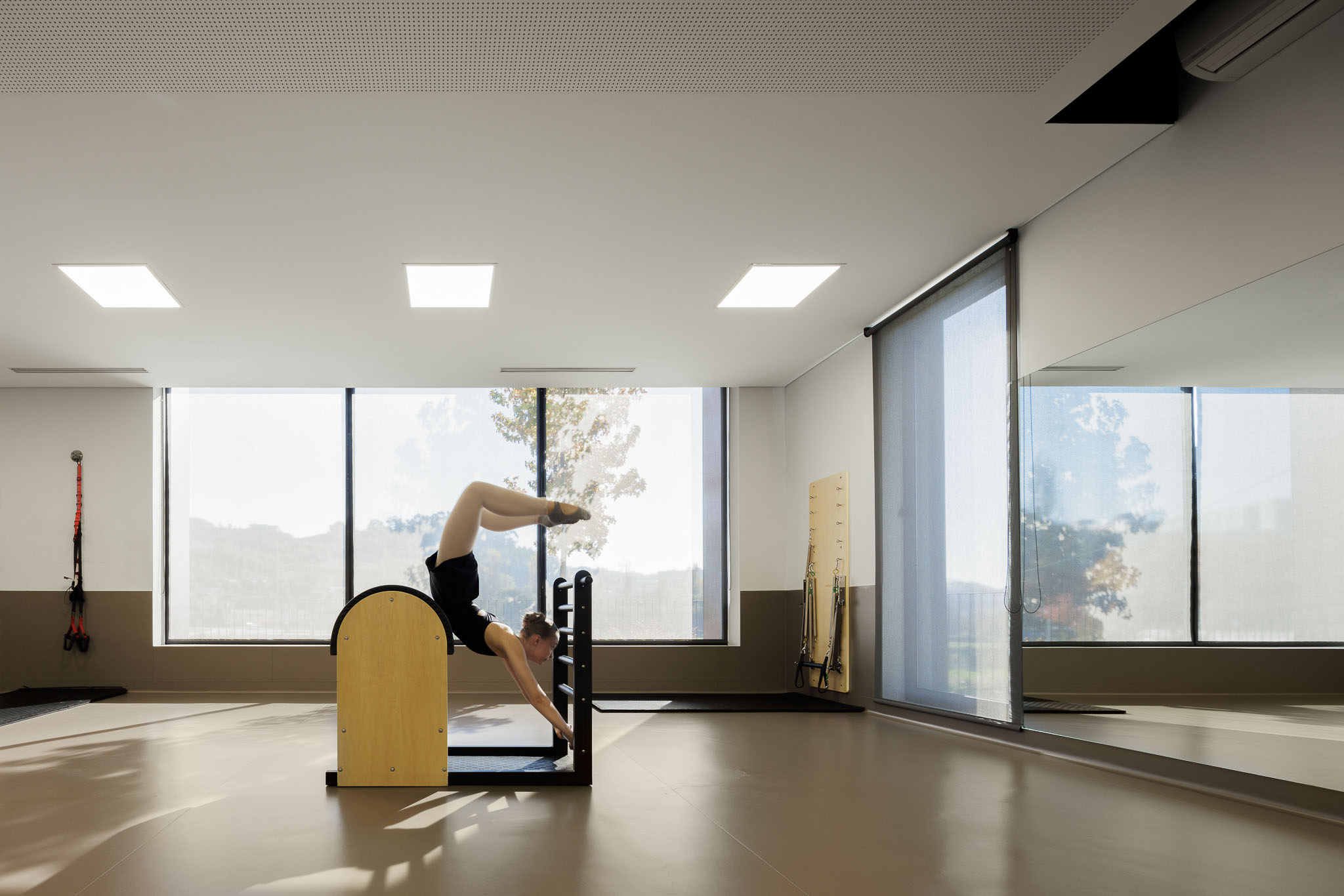 Sala de Pilates: Sala ampla com equipamento de pilates, espelho e janelas grandes. — Clínica de fisioterapia - Fisiminho arquitetura L2C Arquitetura em Braga