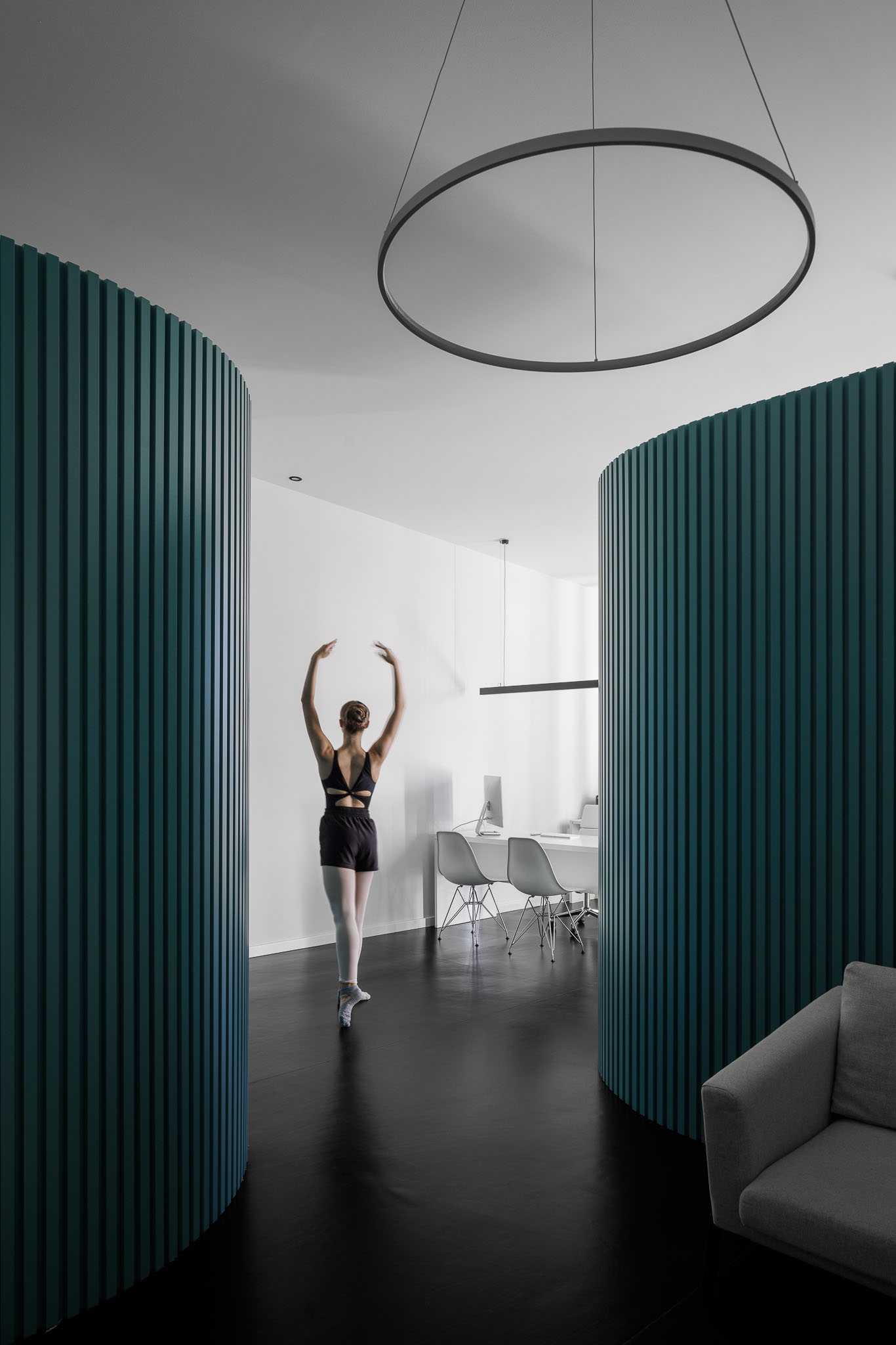 Corredor: Corredor com paredes curvas em ripas verdes, candeeiro circular e sala ao fundo. — Clínica de fisioterapia - Fisiminho arquitetura L2C Arquitetura em Braga