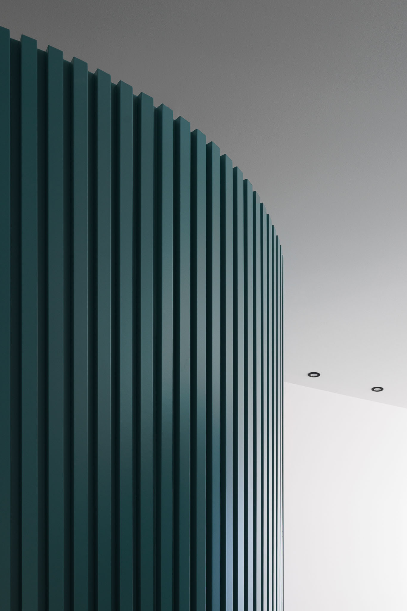 Corredor: Detalhe da parede curva em ripas verdes com candeeiros embutidos no teto. — Clínica de fisioterapia - Fisiminho arquitetura L2C Arquitetura em Braga
