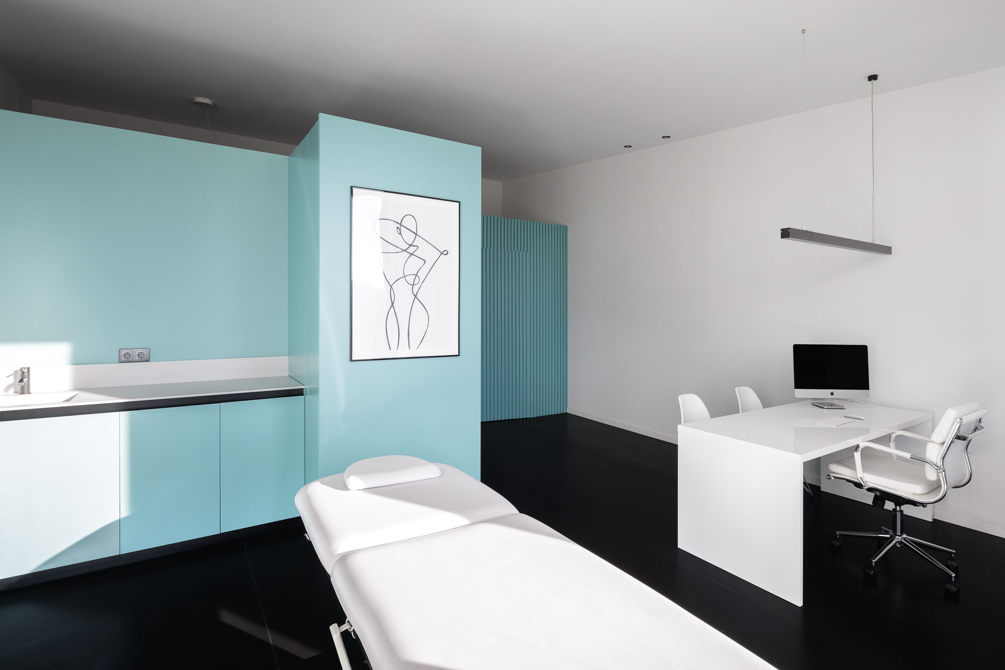Gabinete: Maca branca, lavatório azul, secretária branca e parede em ripas verdes ao fundo. — Clínica de fisioterapia - Fisiminho arquitetura L2C Arquitetura em Braga