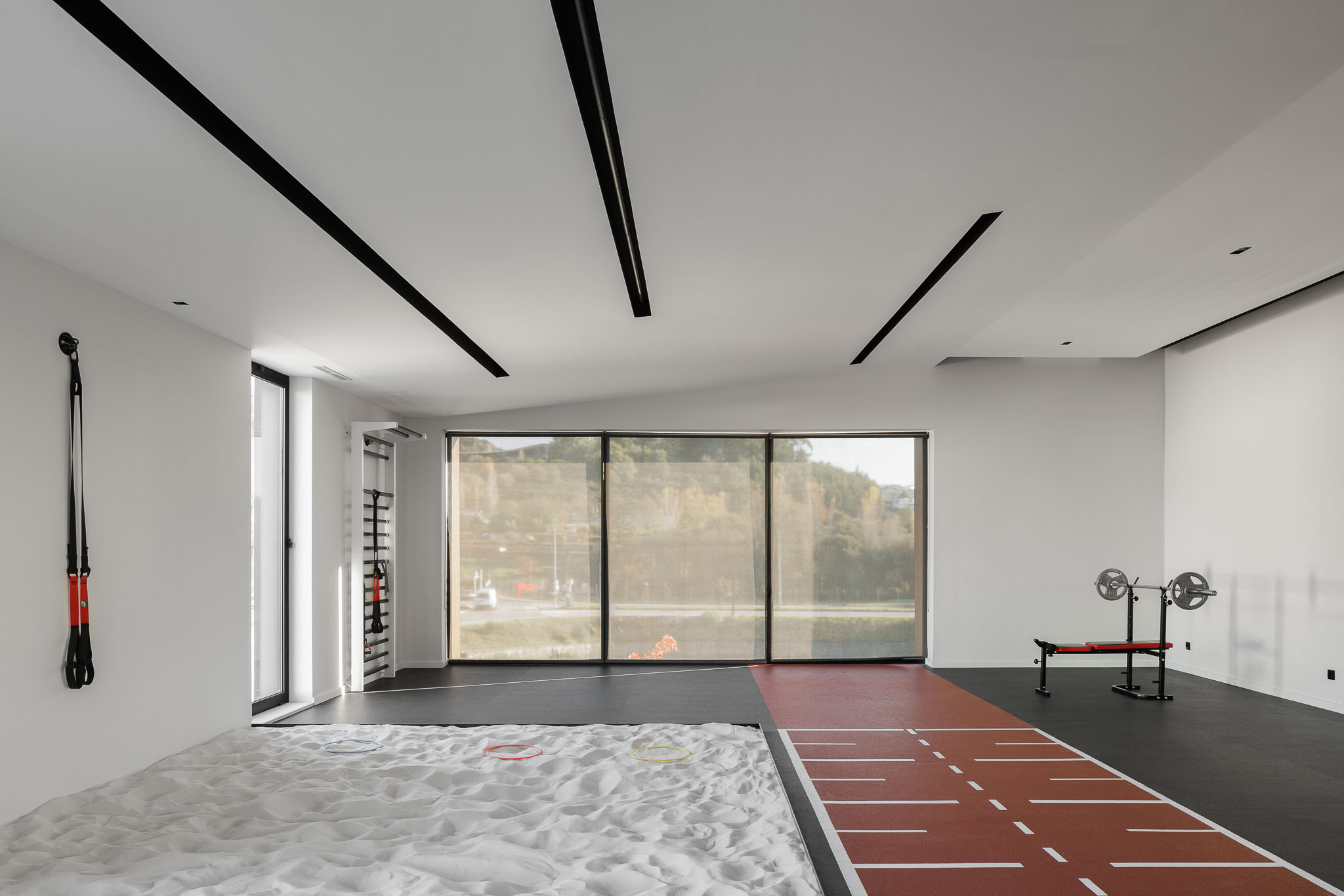 Ginásio: Espaço amplo com equipamentos de treino, caixa de areia e pista de atletismo. — Clínica de fisioterapia - Fisiminho arquitetura L2C Arquitetura em Braga