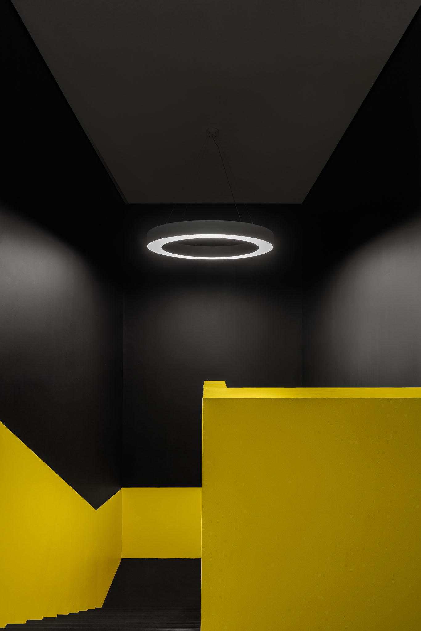 Escadas: Detalhe das escadas pretas com paredes amarelas e candeeiro circular suspenso. — Clínica de fisioterapia - Fisiminho arquitetura L2C Arquitetura em Braga