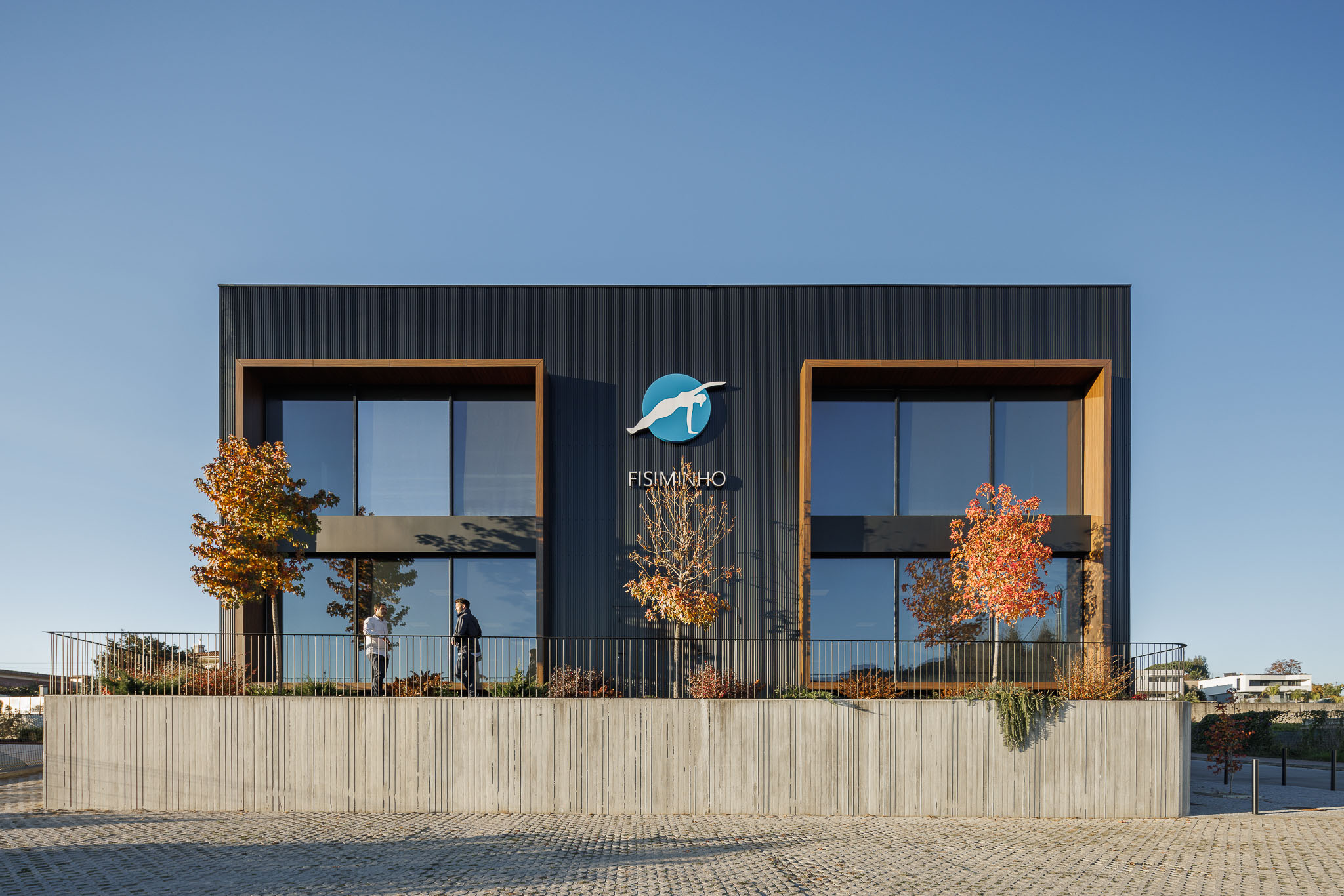 Fachada: Edifício com revestimento metálico preto, janelas amplas e logótipo "Fisiminho". — Clínica de fisioterapia - Fisiminho arquitetura L2C Arquitetura em Braga
