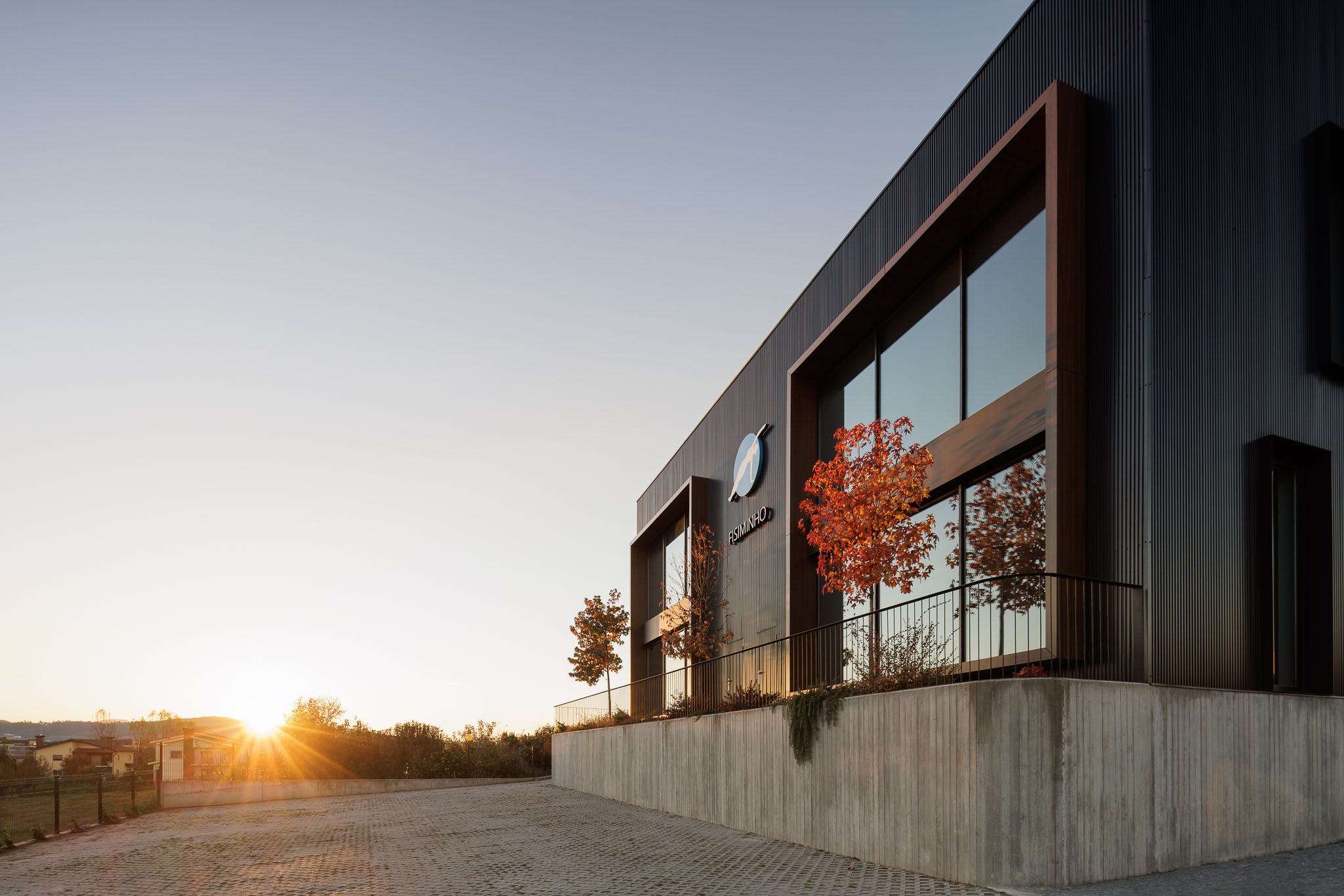 Fachada: Edifício com revestimento metálico preto, janelas amplas e paisagismo. — Clínica de fisioterapia - Fisiminho arquitetura L2C Arquitetura em Braga