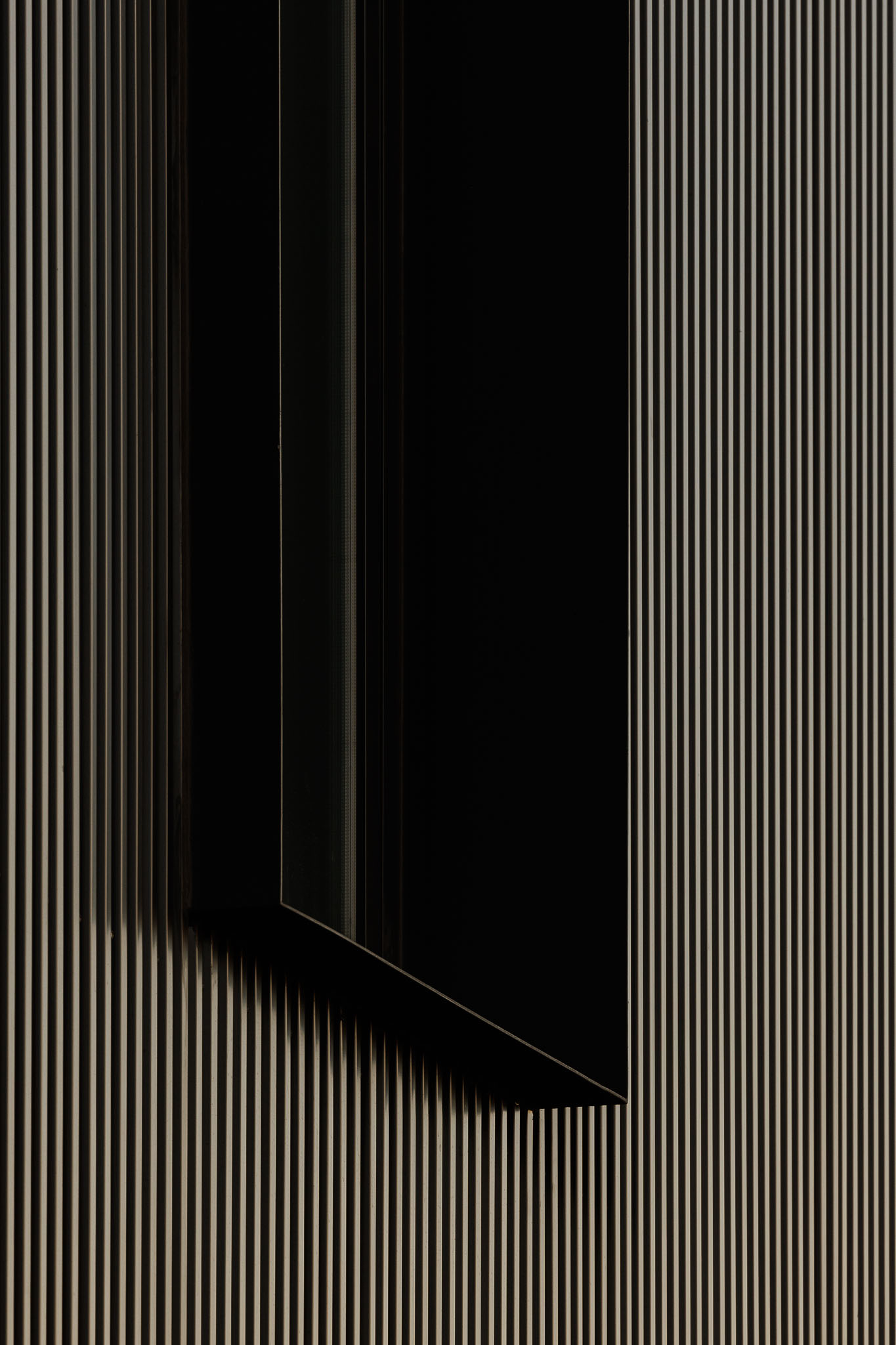 Fachada: Detalhe de janela vertical em fachada metálica com reflexos de luz. — Clínica de fisioterapia - Fisiminho arquitetura L2C Arquitetura em Braga