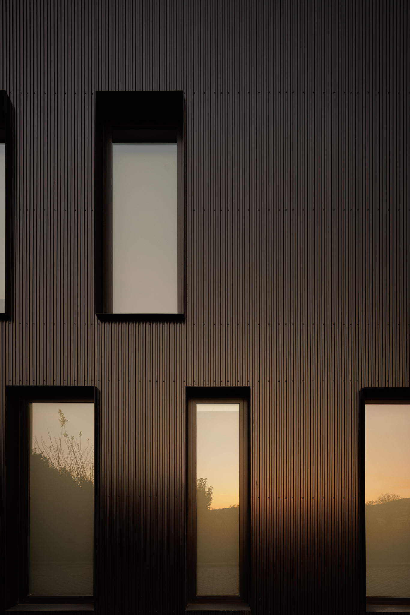Fachada: Detalhe de janelas verticais em fachada metálica preta ao entardecer. — Clínica de fisioterapia - Fisiminho arquitetura L2C Arquitetura em Braga