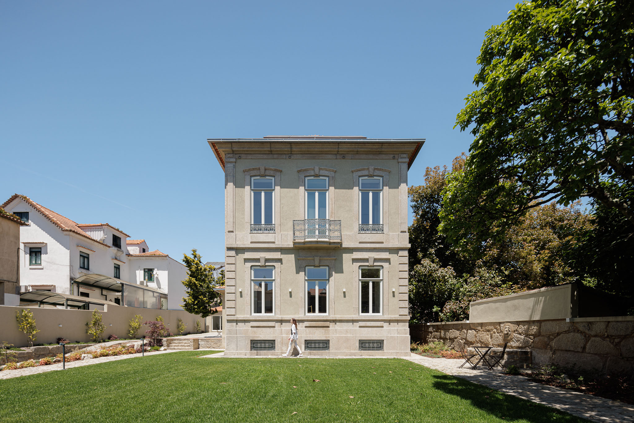 Exterior: Fachada principal da casa com jardim relvado, árvores e céu azul. — Casa Kala arquitetura Ren Ito em Porto