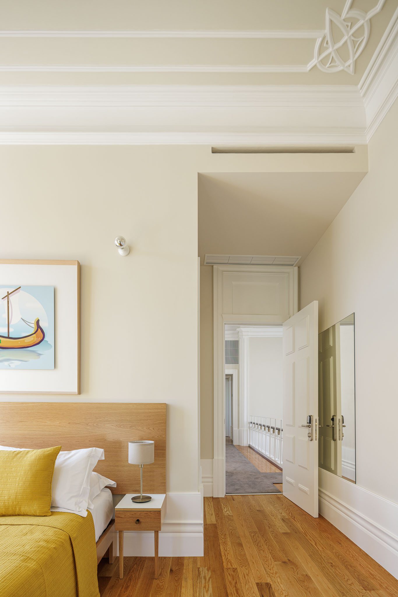 Quarto: Cama com roupa de cama amarela, mesa de cabeceira em madeira, porta branca e pavimento de madeira. — Casa Kala arquitetura Ren Ito em Porto