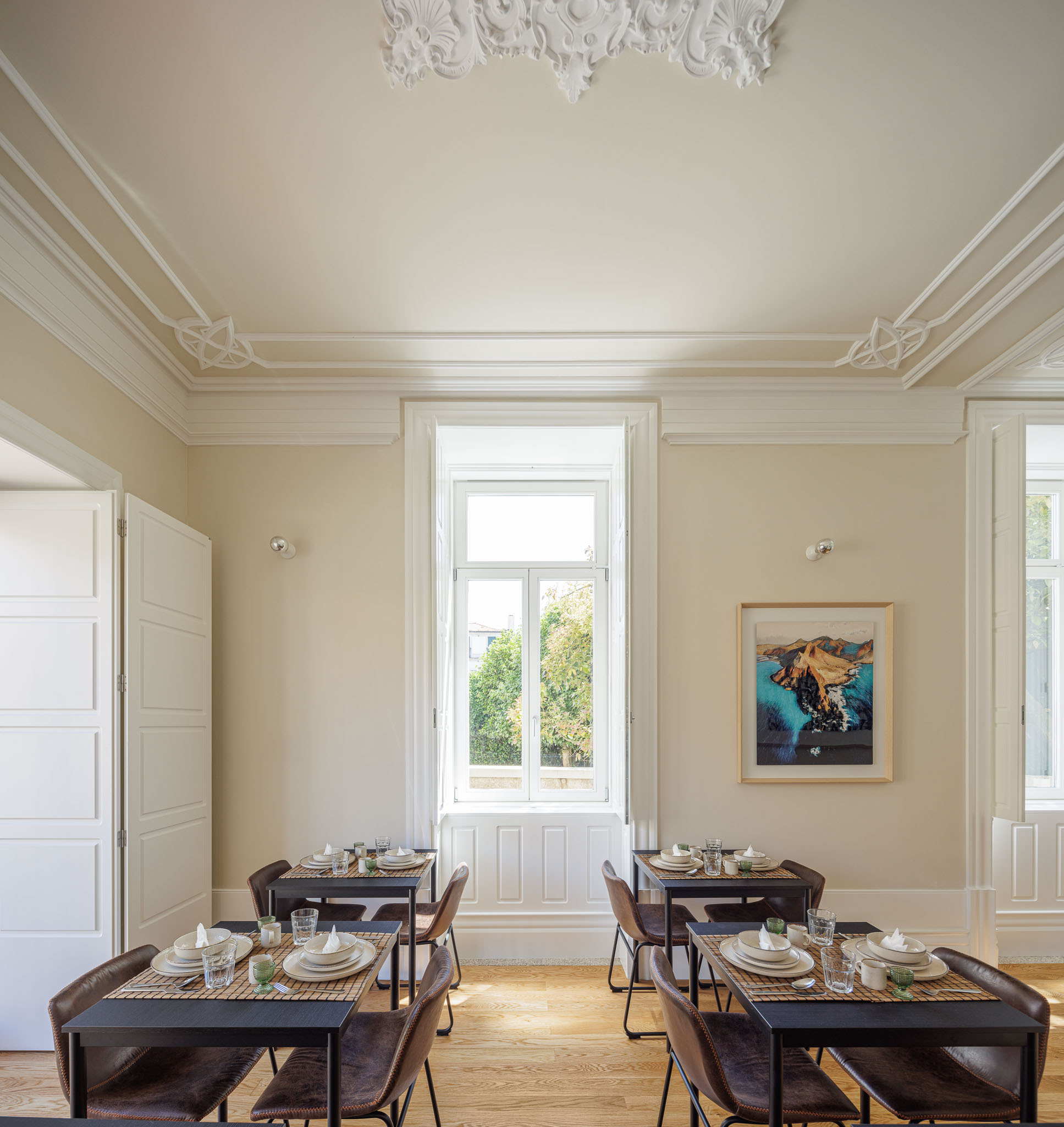 Sala de jantar: Mesas pretas com cadeiras de couro castanho, pavimento de madeira e tecto com molduras clássicas. — Casa Kala arquitetura Ren Ito em Porto