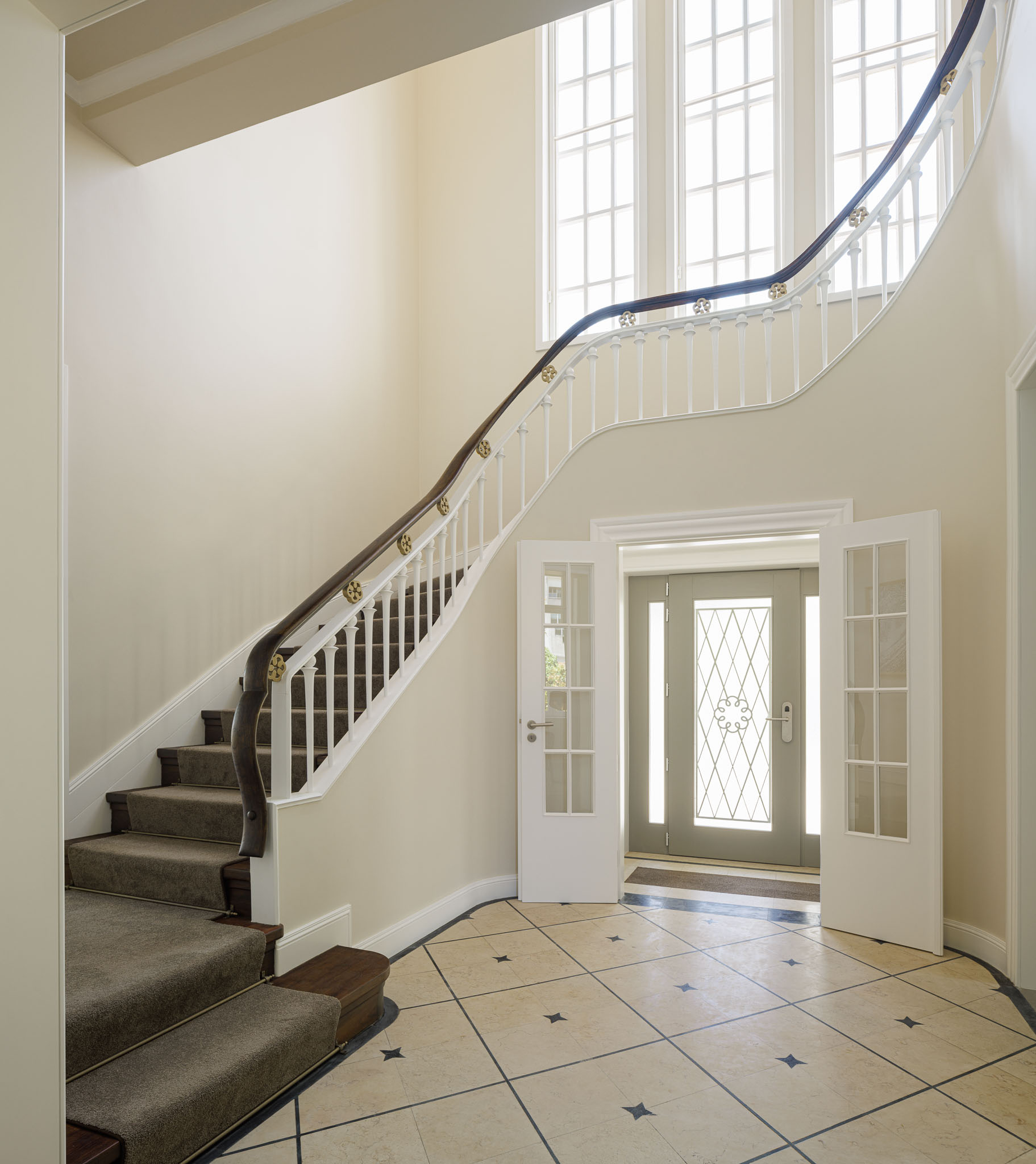Hall de entrada: Escadaria curva com corrimão de madeira e alcatifa, pavimento em mosaico e porta de entrada envidraçada. — Casa Kala arquitetura Ren Ito em Porto