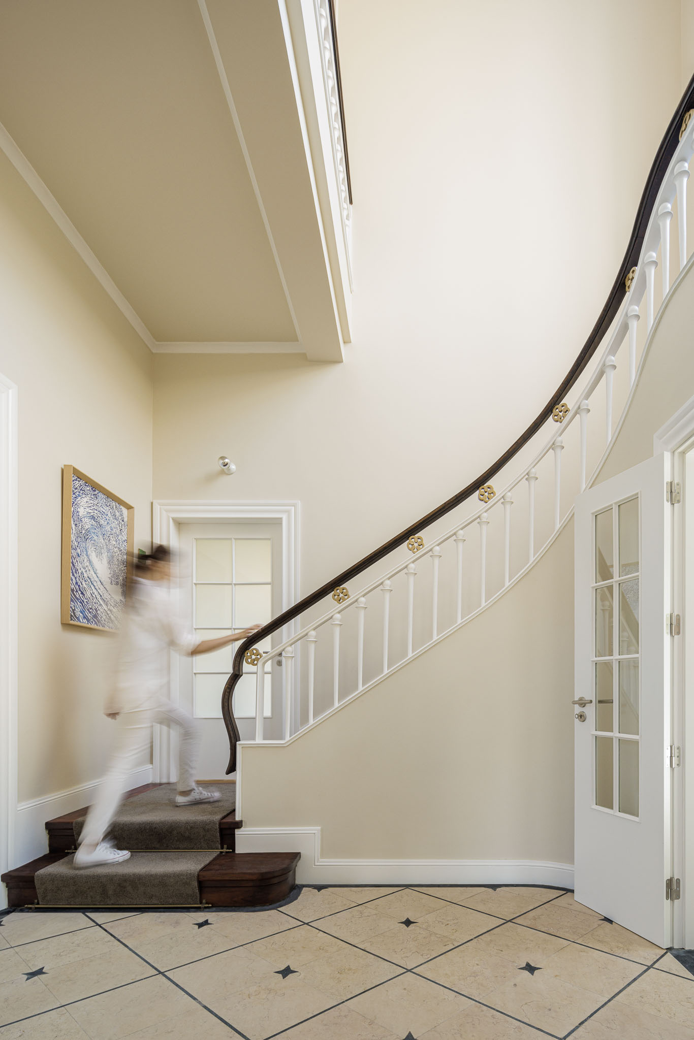 Hall de entrada: Escadaria curva com corrimão de madeira e alcatifa, pavimento em mosaico e paredes bege. — Casa Kala arquitetura Ren Ito em Porto