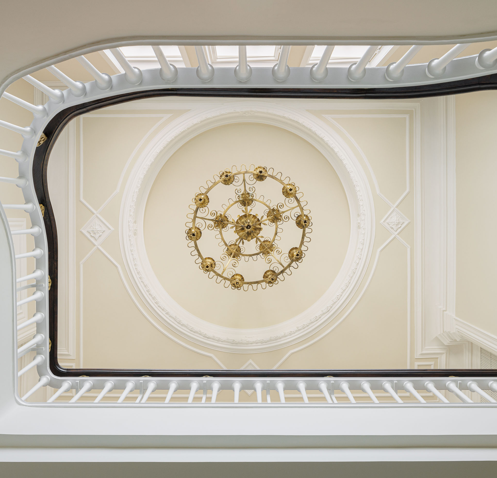 Escadaria: Vista do tecto com candeeiro dourado, molduras decorativas e corrimão da escadaria. — Casa Kala arquitetura Ren Ito em Porto