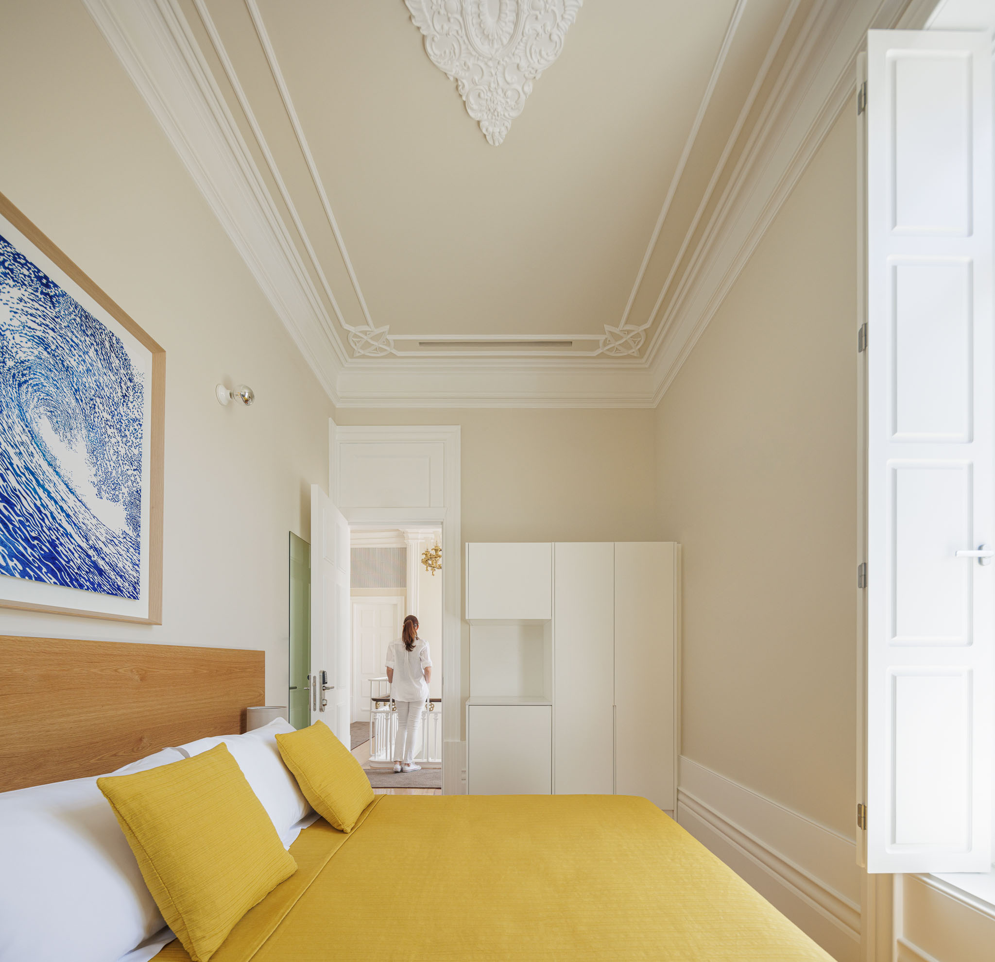 Quarto: Cama com roupa de cama amarela, roupeiro branco embutido e tecto com molduras clássicas. — Casa Kala arquitetura Ren Ito em Porto