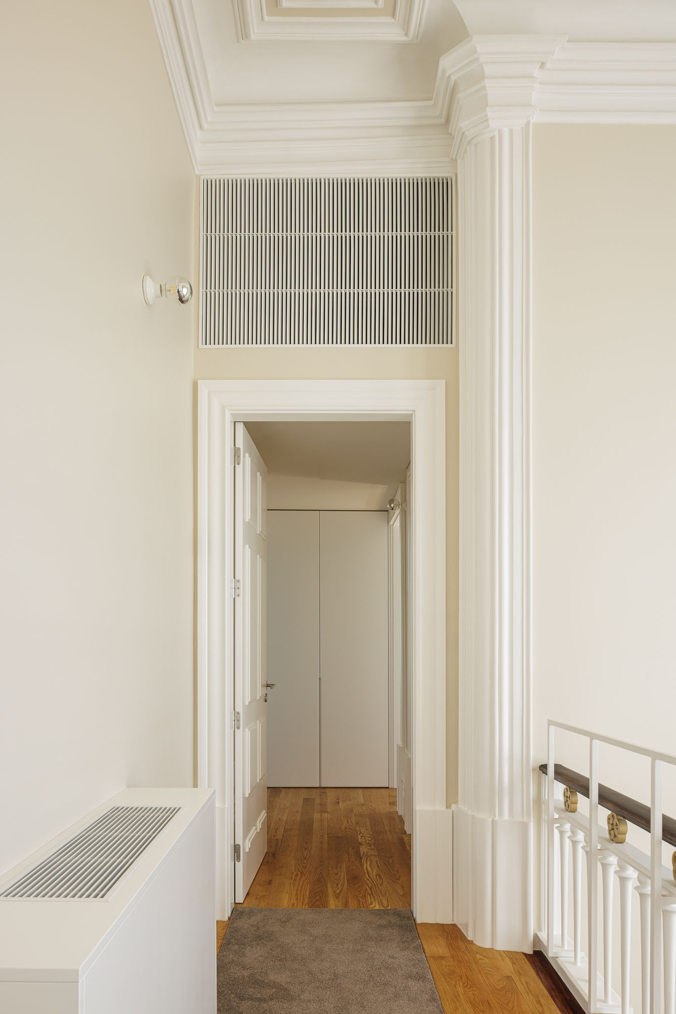 Hall: Porta branca, coluna decorativa, grelha de ventilação e pavimento de madeira com alcatifa. — Casa Kala arquitetura Ren Ito em Porto