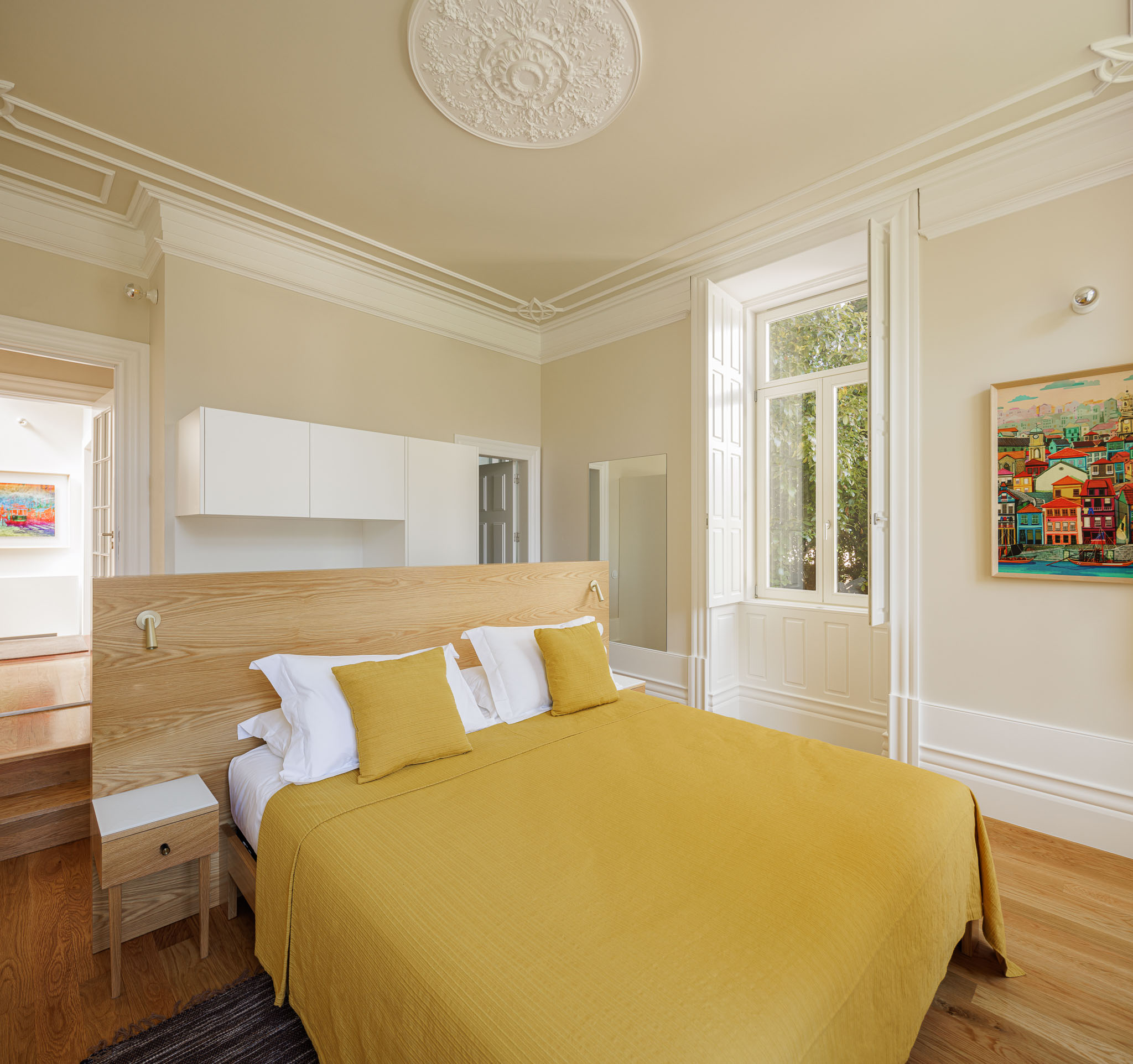 Quarto: Cama com roupa de cama amarela, mesa de cabeceira em madeira e tecto com molduras clássicas. — Casa Kala arquitetura Ren Ito em Porto