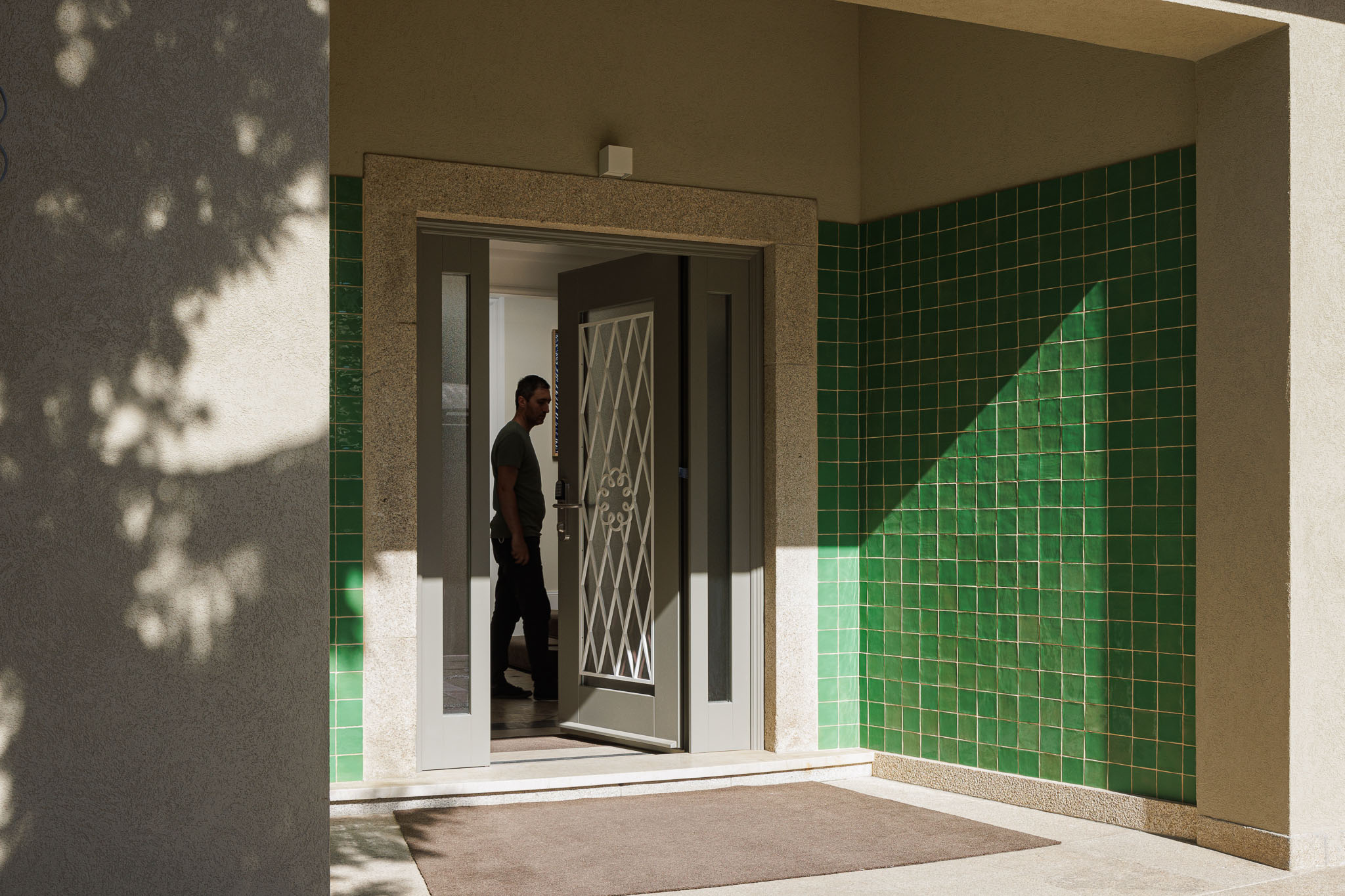 Entrada: Porta de entrada com azulejos verdes na parede e tapete no chão. — Casa Kala arquitetura Ren Ito em Porto