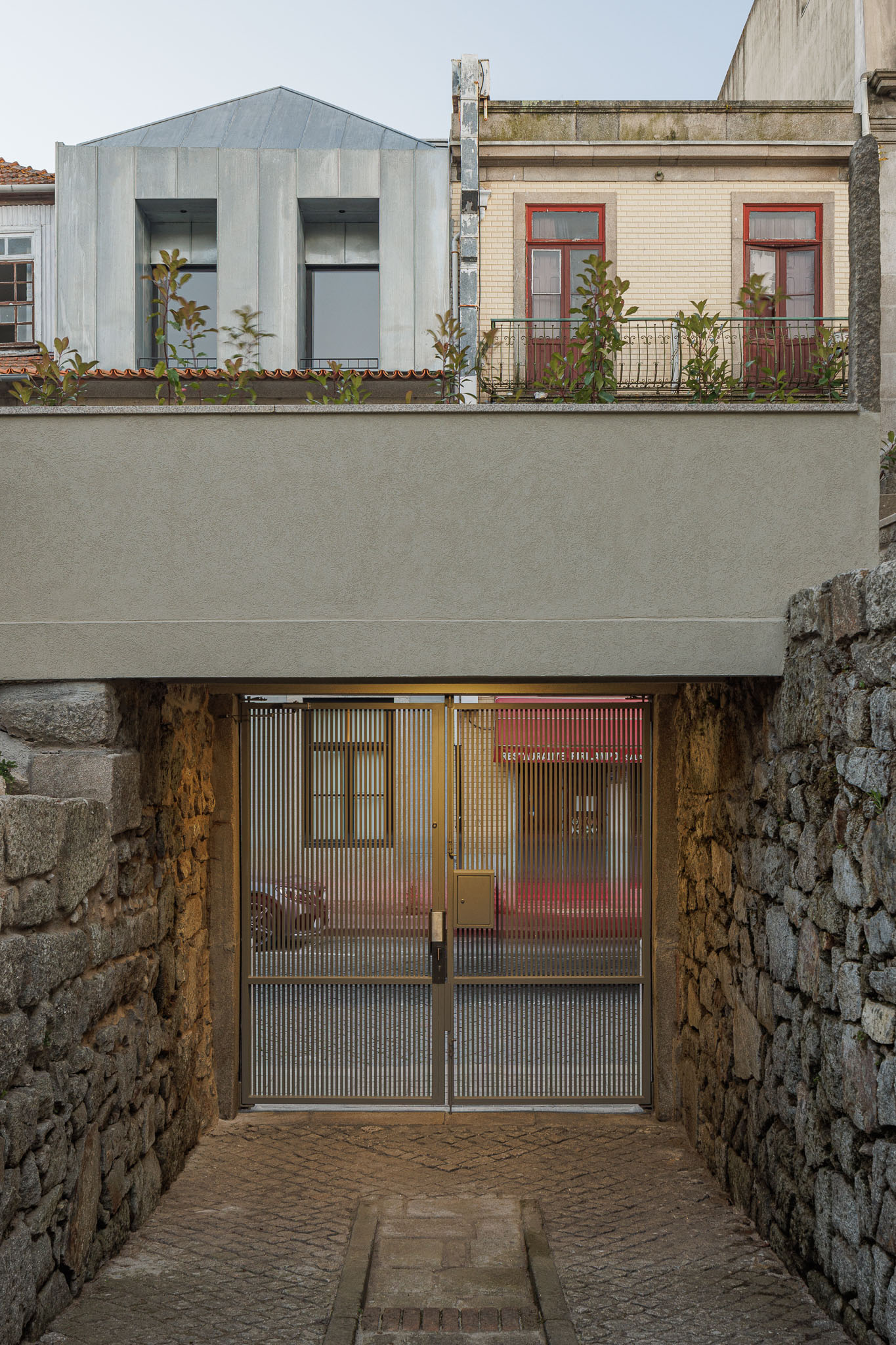 Exterior: Portão metálico com paredes de pedra rústica. — Casa Kala arquitetura Ren Ito em Porto