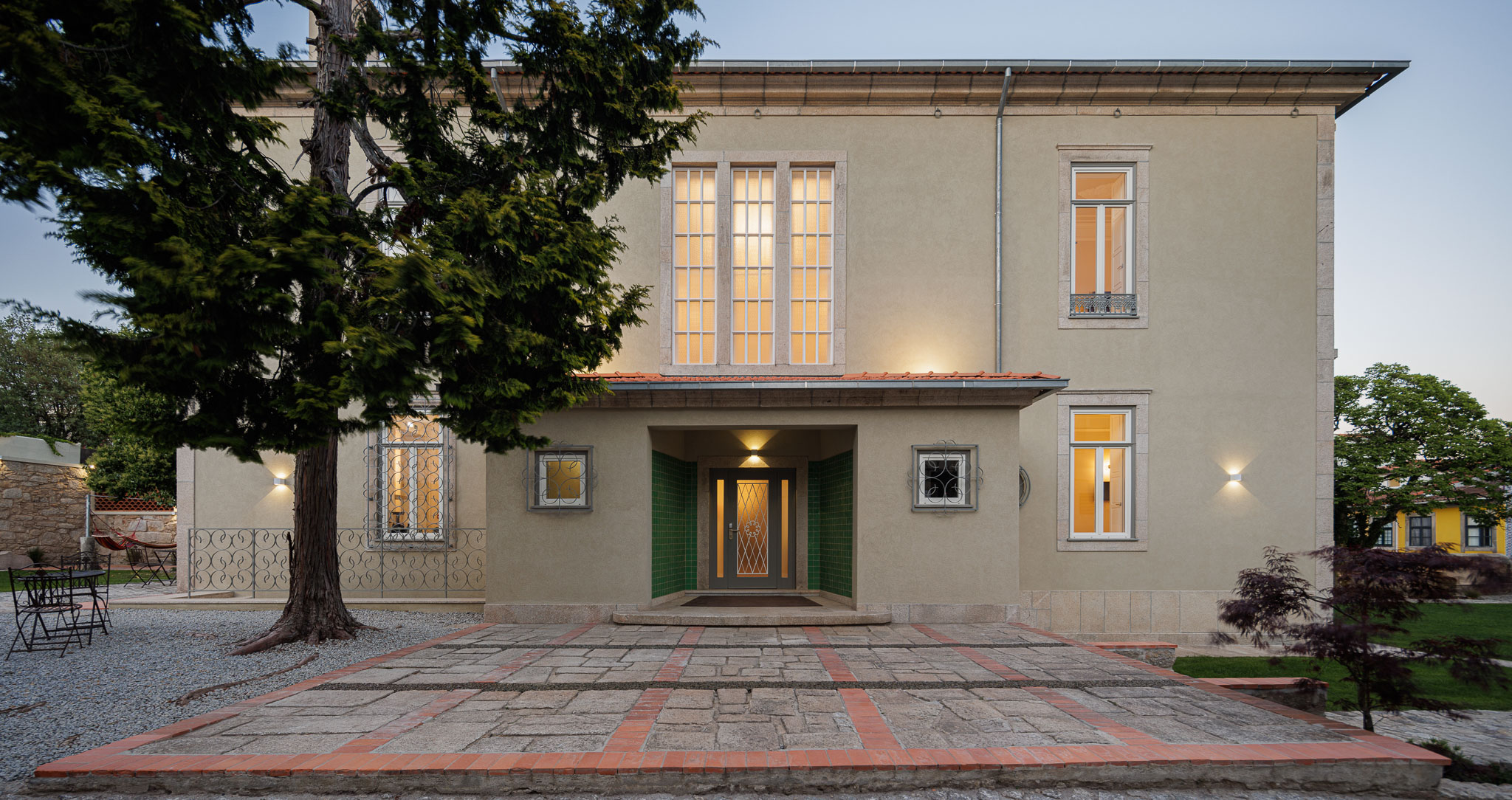 Exterior: Fachada frontal da casa com jardim e árvores. — Casa Kala arquitetura Ren Ito em Porto
