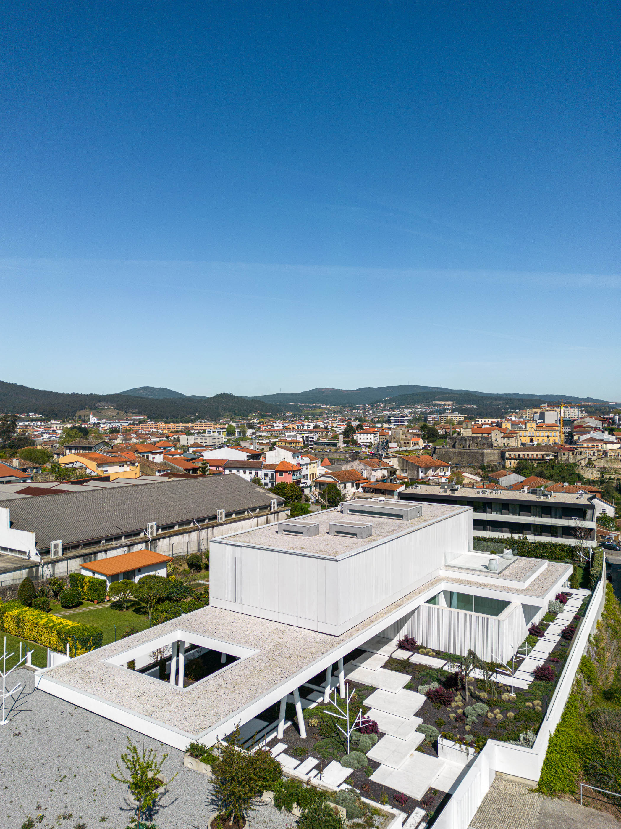 Cobertura: Vista aérea da moradia minimalista branca com telhado ajardinado e piscina, integrada na paisagem urbana de Barcelos. — Riscowhite arquitetura Risco Singular em Barcelos