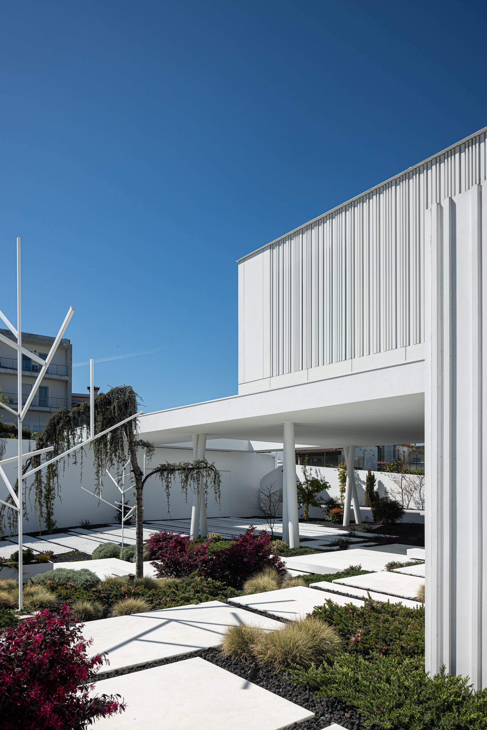 Jardim: Moradia branca com jardim minimalista, escada em caracol e estrutura metálica decorativa. — Riscowhite arquitetura Risco Singular em Barcelos