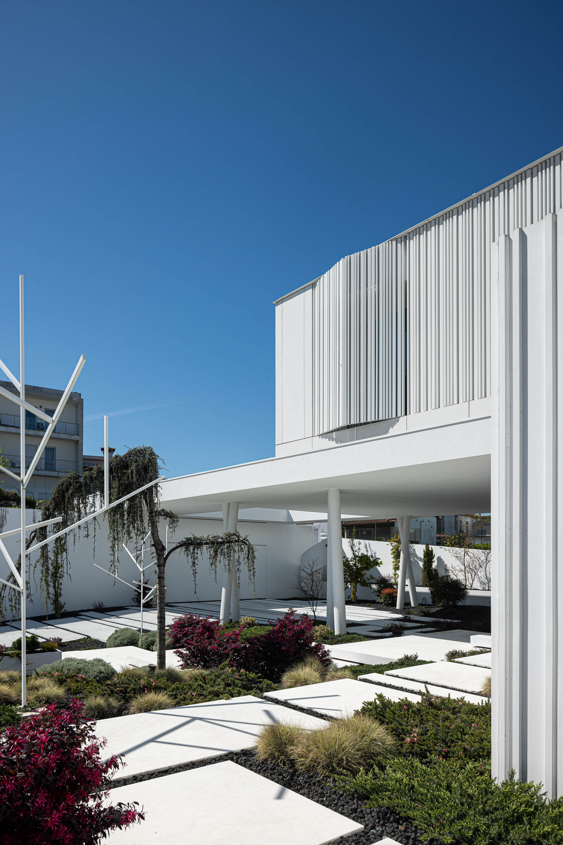 Jardim: Moradia branca com jardim minimalista, escada em caracol e estrutura metálica decorativa. — Riscowhite arquitetura Risco Singular em Barcelos