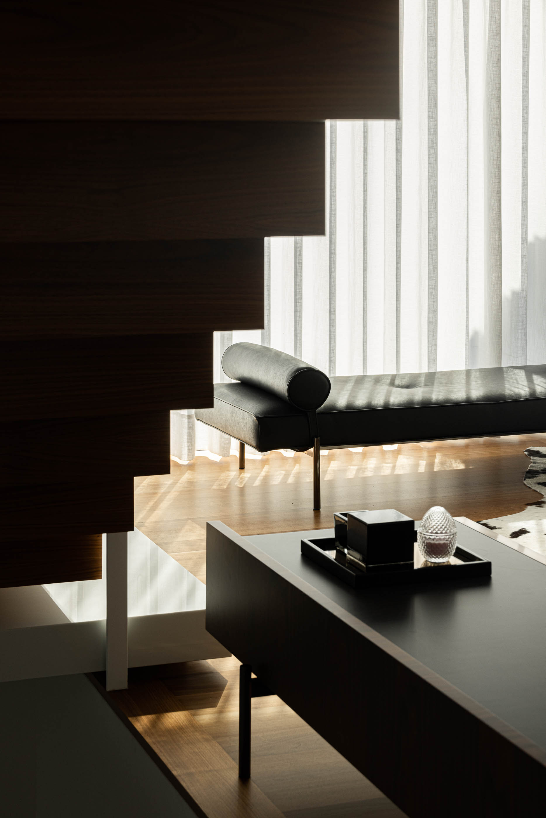 Hall de entrada: Detalhe da escada em madeira, sofá preto e mesa lateral com objetos decorativos. — Riscowhite arquitetura Risco Singular em Barcelos