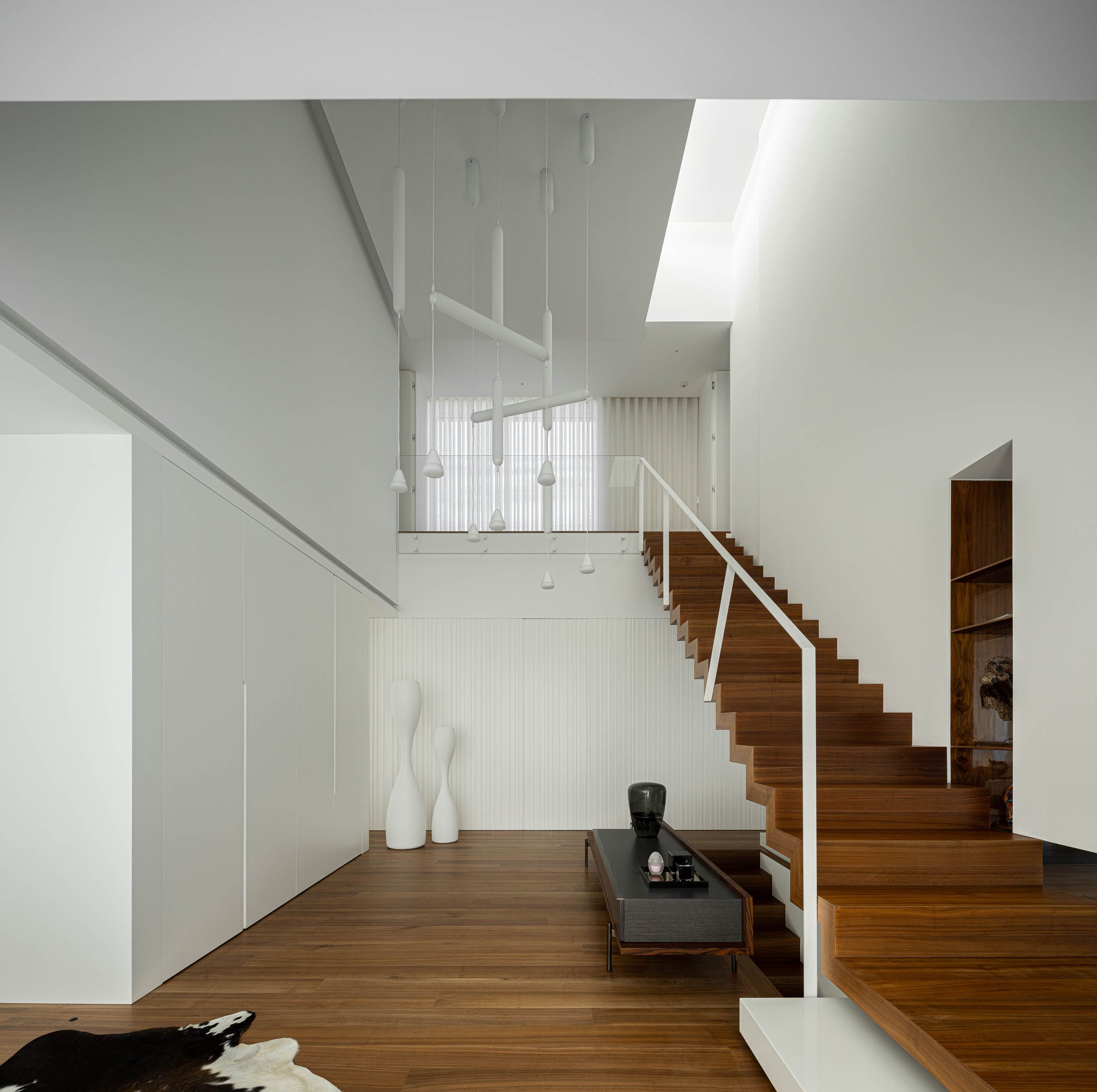 Hall de entrada: Espaço amplo com escada em madeira, candeeiros suspensos e decoração minimalista branca. — Riscowhite arquitetura Risco Singular em Barcelos