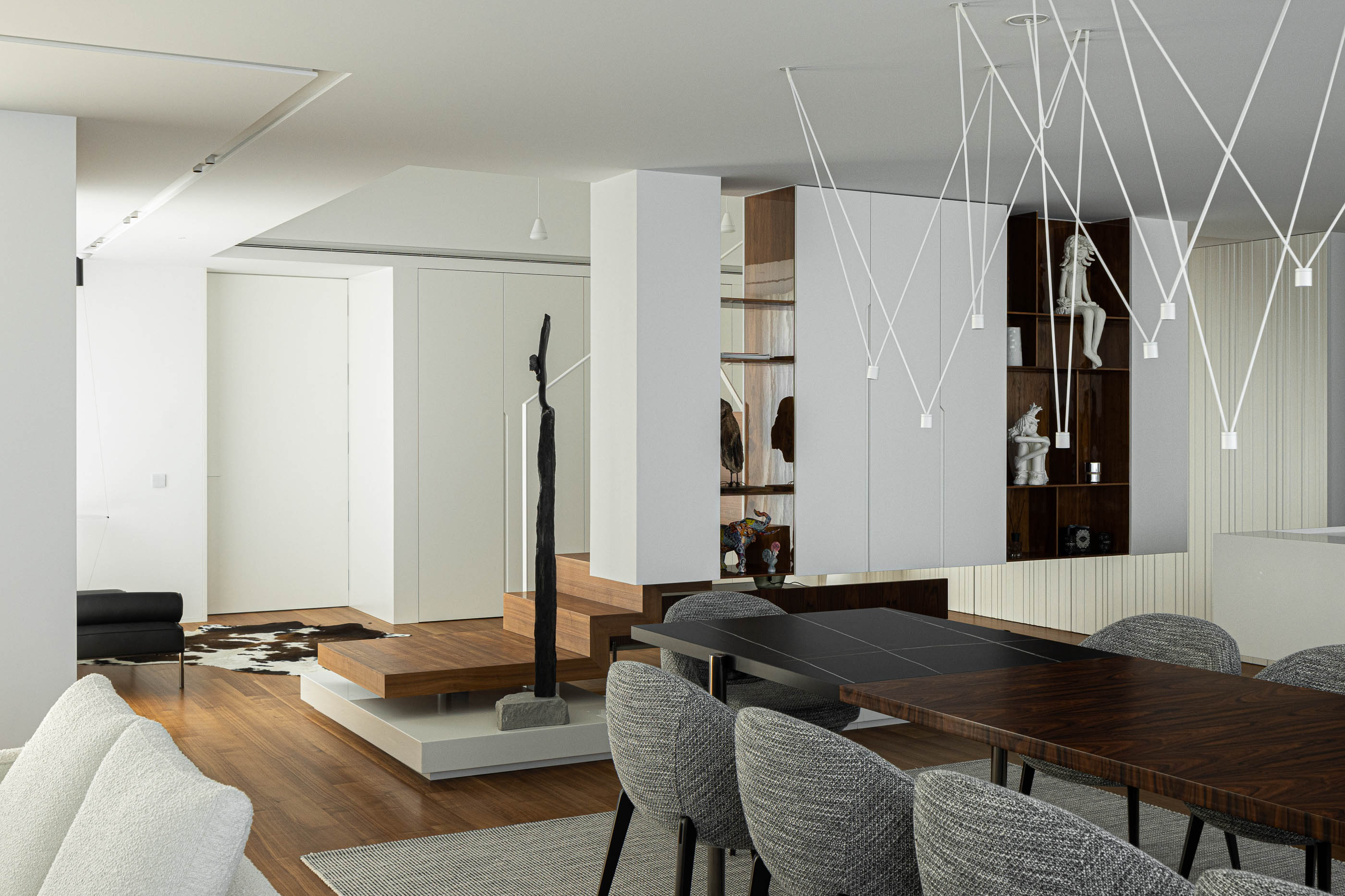 Sala de jantar: Vista ampla da sala com escada, mesa de jantar, cadeiras cinzentas e candeeiro moderno. — Riscowhite arquitetura Risco Singular em Barcelos