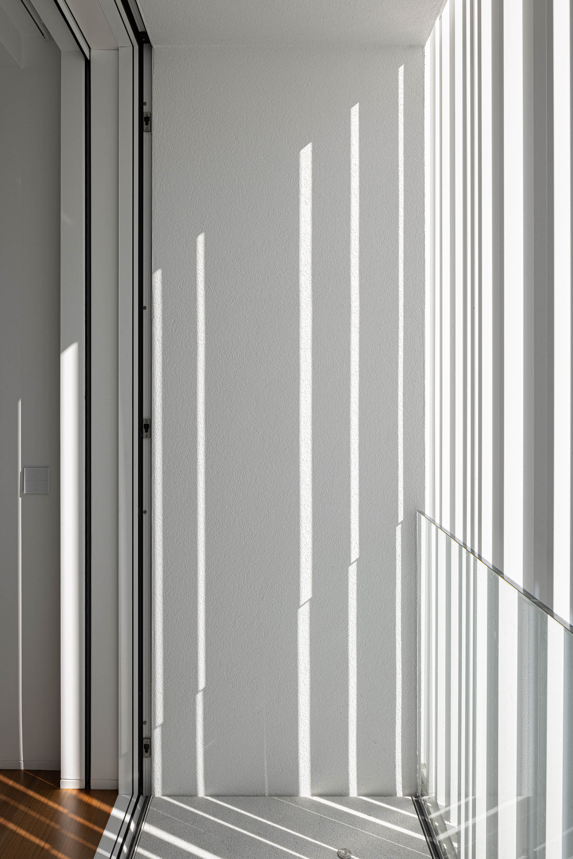 Escada: Detalhe da escada com luz natural filtrada por persianas verticais e guarda em vidro. — Riscowhite arquitetura Risco Singular em Barcelos