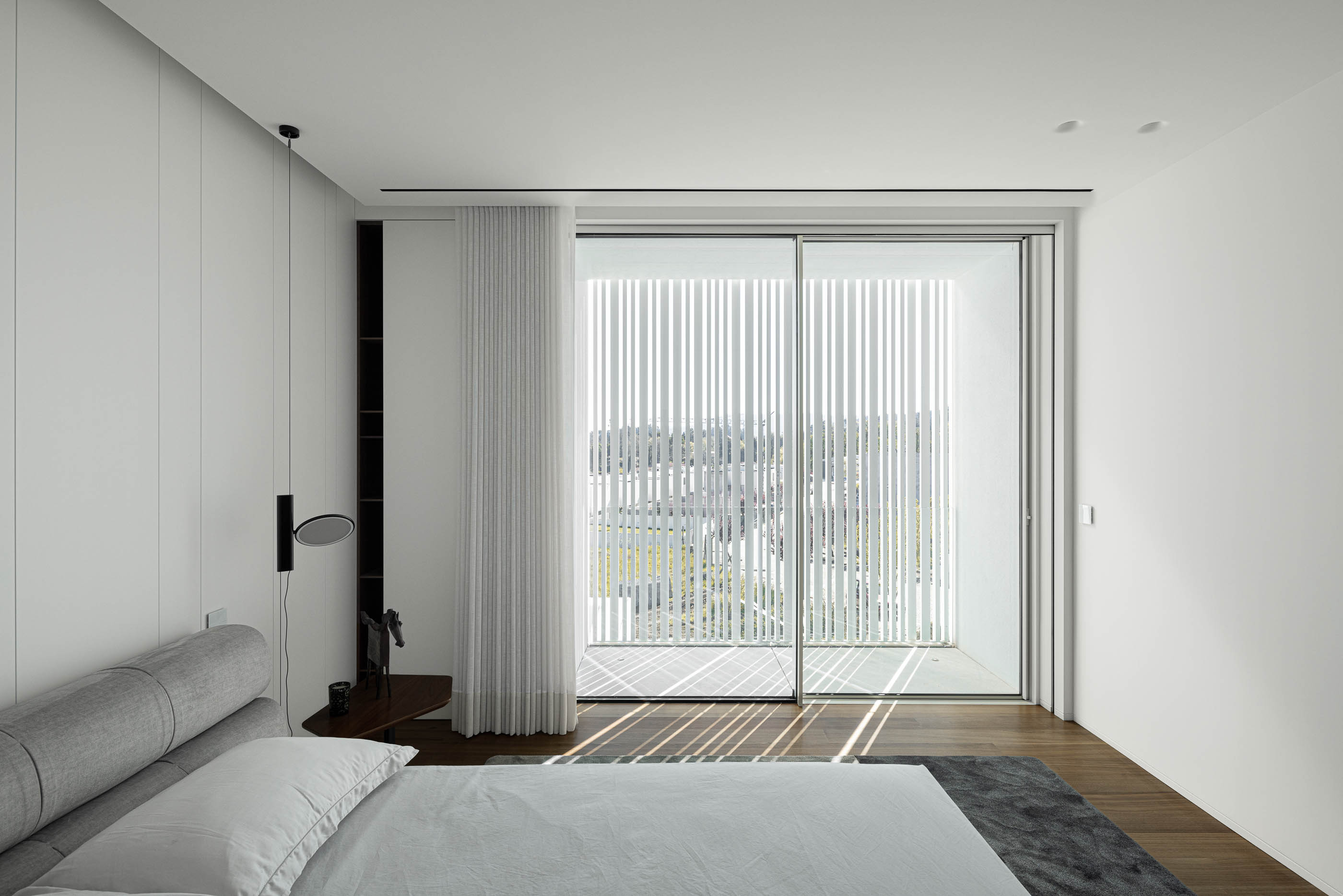Quarto: Cama com cabeceira cinzenta, cortinas verticais e roupeiro branco em quarto minimalista. — Riscowhite arquitetura Risco Singular em Barcelos