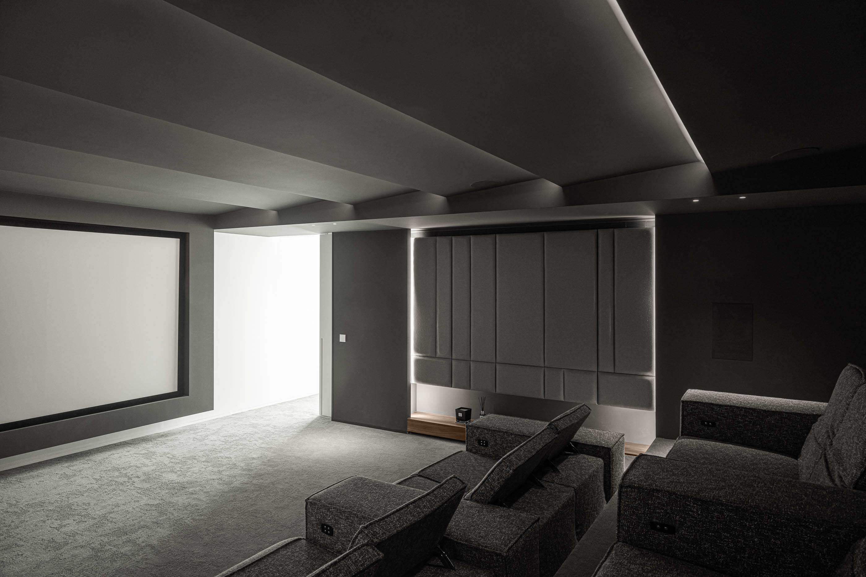 Sala de cinema: Espaço escuro com sofás modulares cinzentos e ecrã de projeção. — Riscowhite arquitetura Risco Singular em Barcelos