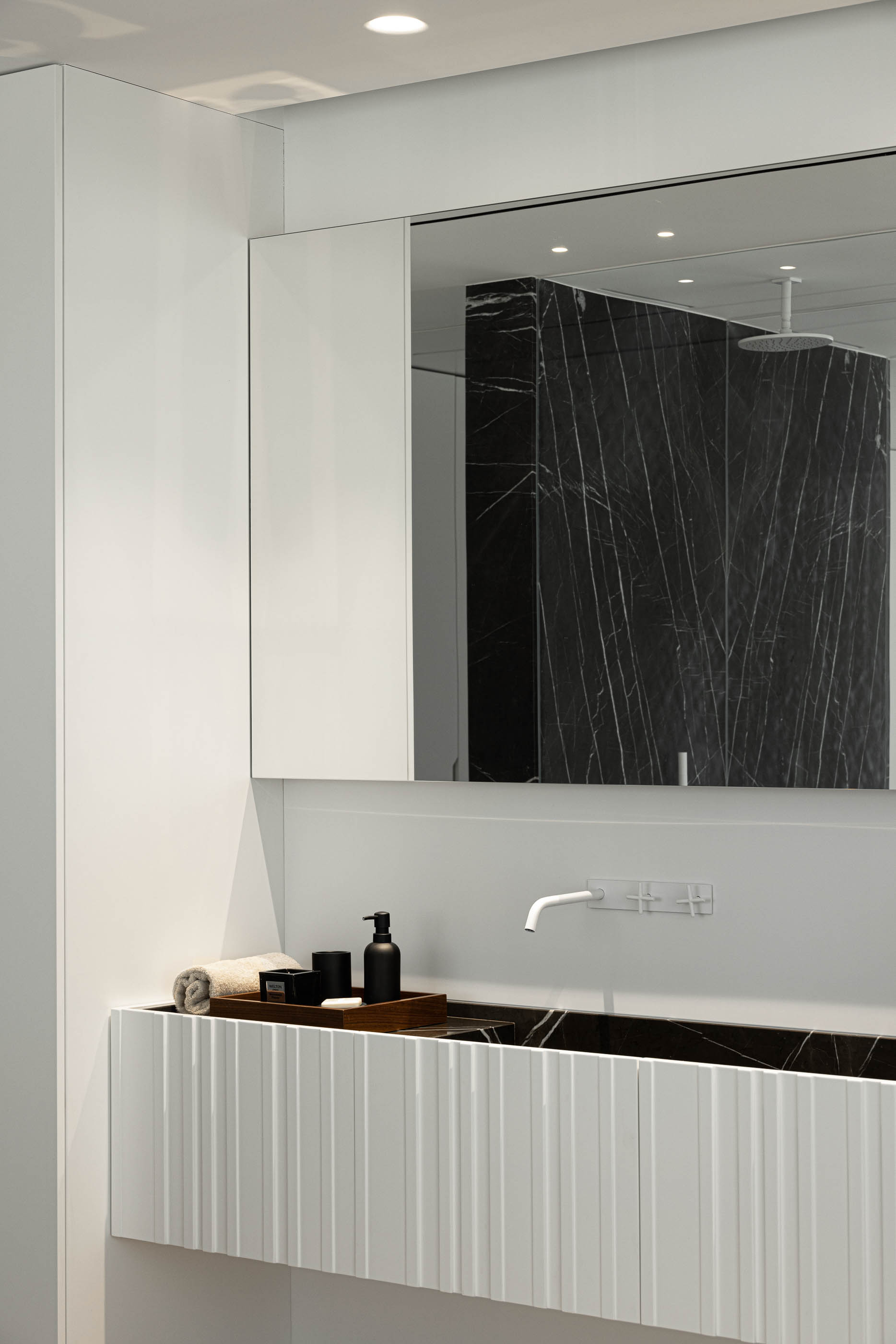 Casa de banho: Lavatório branco com torneira minimalista e espelho refletindo o duche em mármore preto. — Riscowhite arquitetura Risco Singular em Barcelos