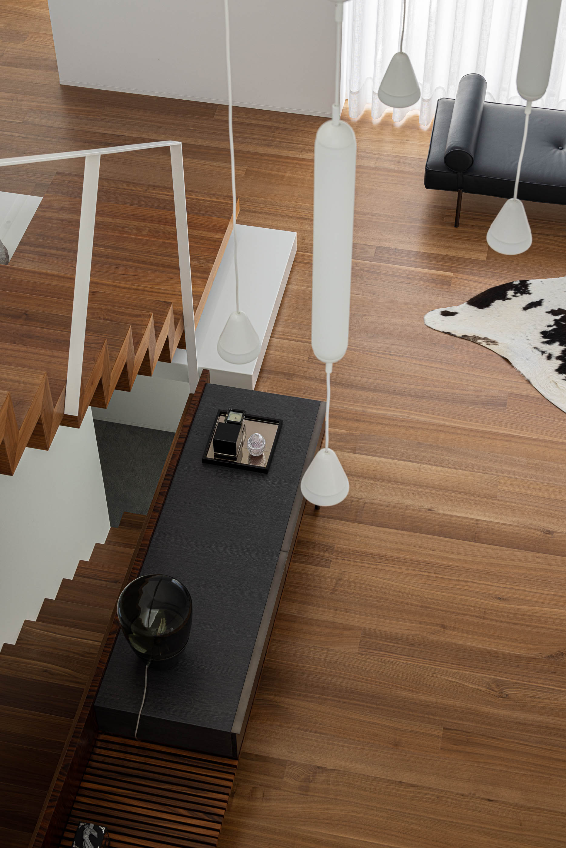 Hall de entrada: Vista superior da escada, candeeiros suspensos e zona de estar com sofá preto. — Riscowhite arquitetura Risco Singular em Barcelos