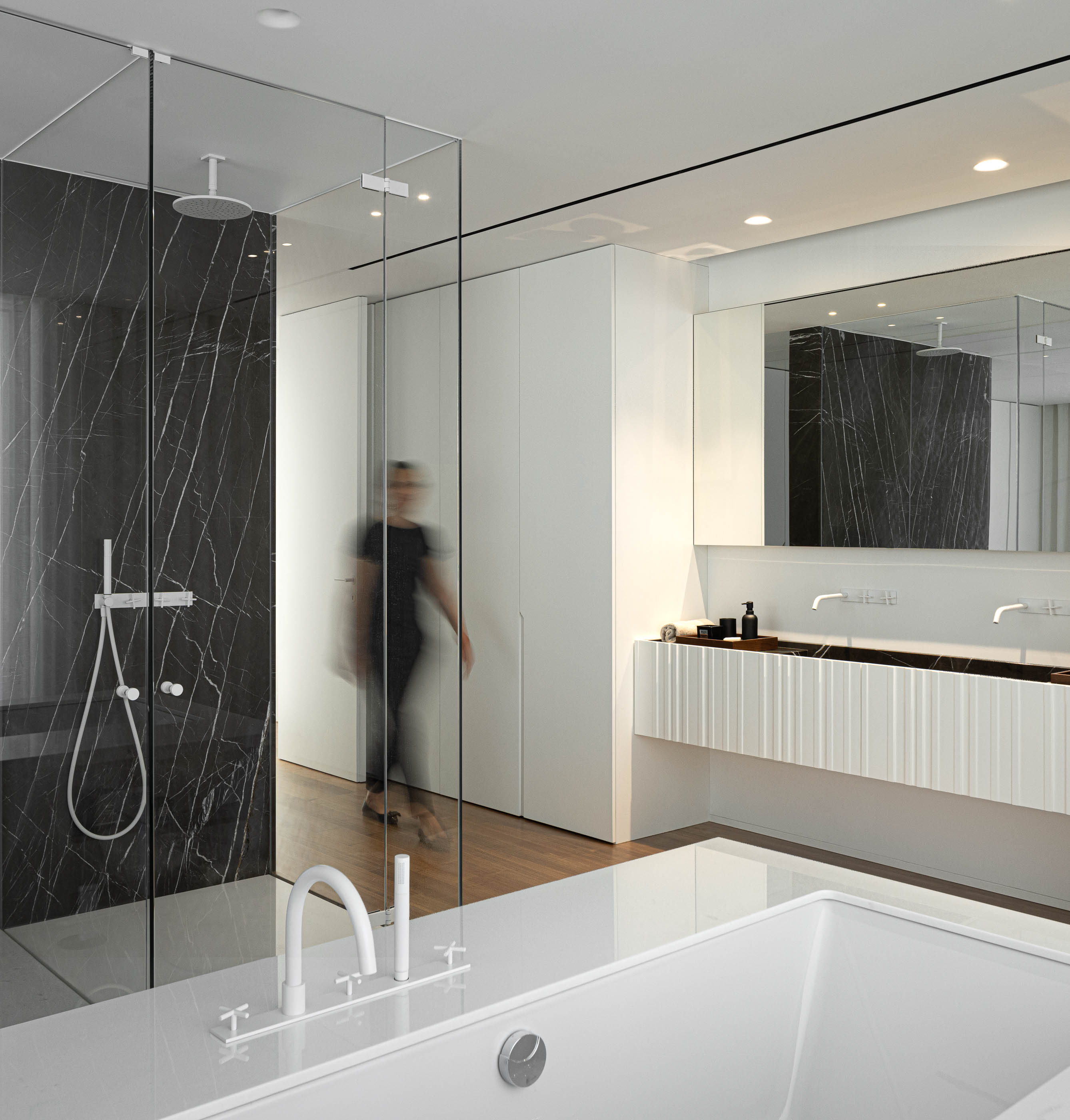 Casa de banho: Banheira branca, duche em mármore preto e lavatório duplo em casa de banho minimalista. — Riscowhite arquitetura Risco Singular em Barcelos
