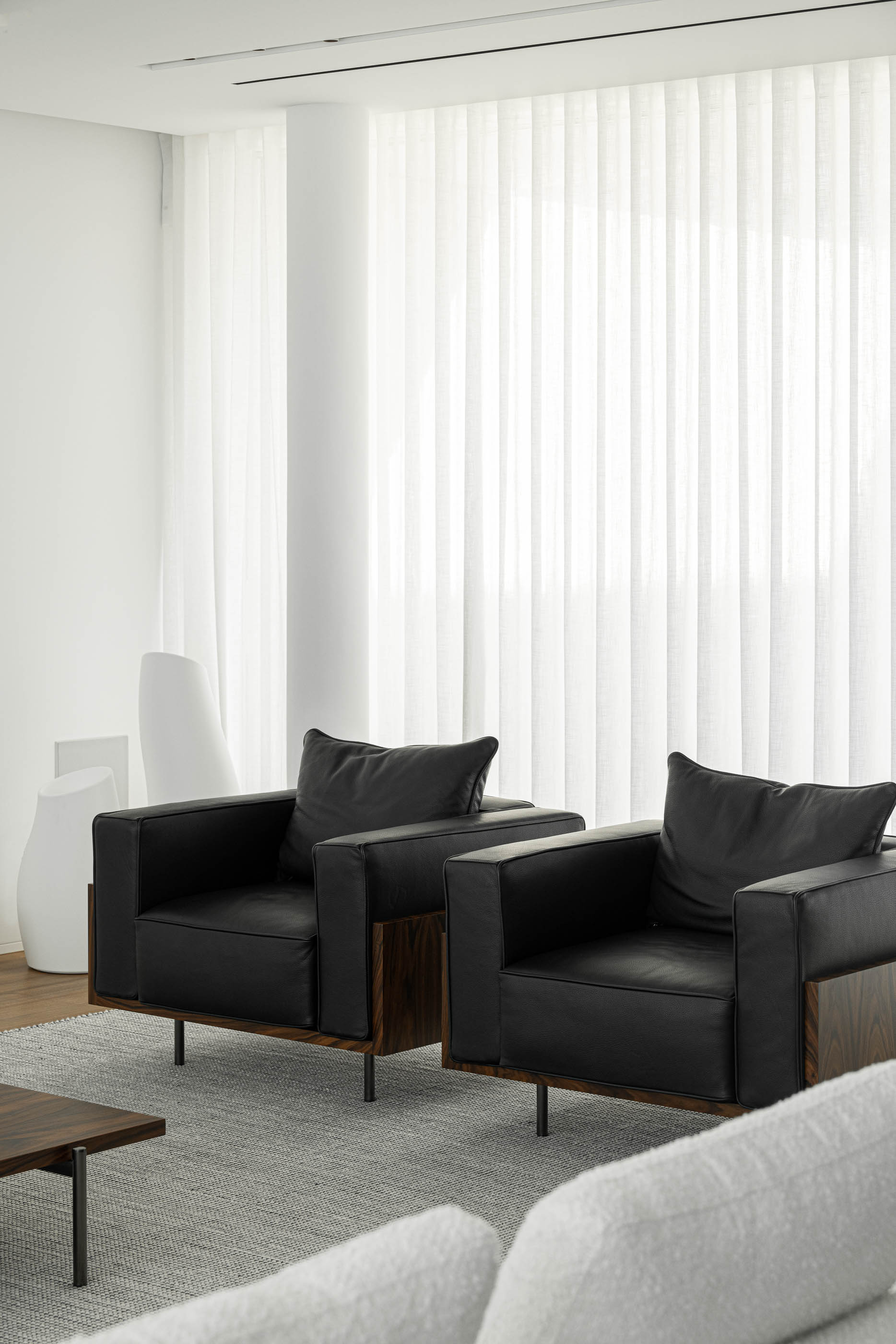 Sala de estar: Poltronas pretas em pele e alcatifa cinzenta, com cortinas brancas ao fundo. — Riscowhite arquitetura Risco Singular em Barcelos