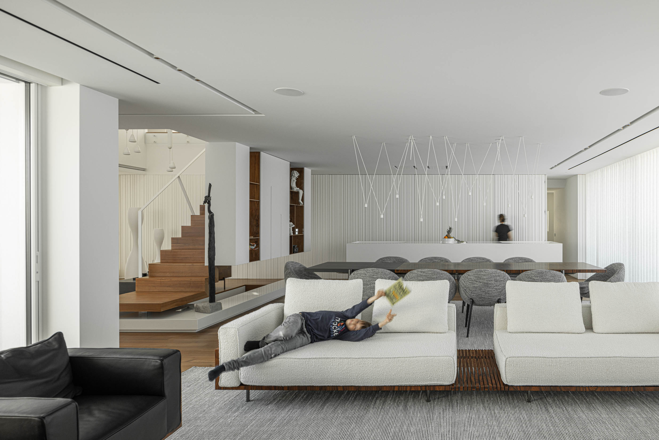 Sala de estar: Vista ampla da sala com sofás brancos, mesa de jantar e escada em madeira. — Riscowhite arquitetura Risco Singular em Barcelos