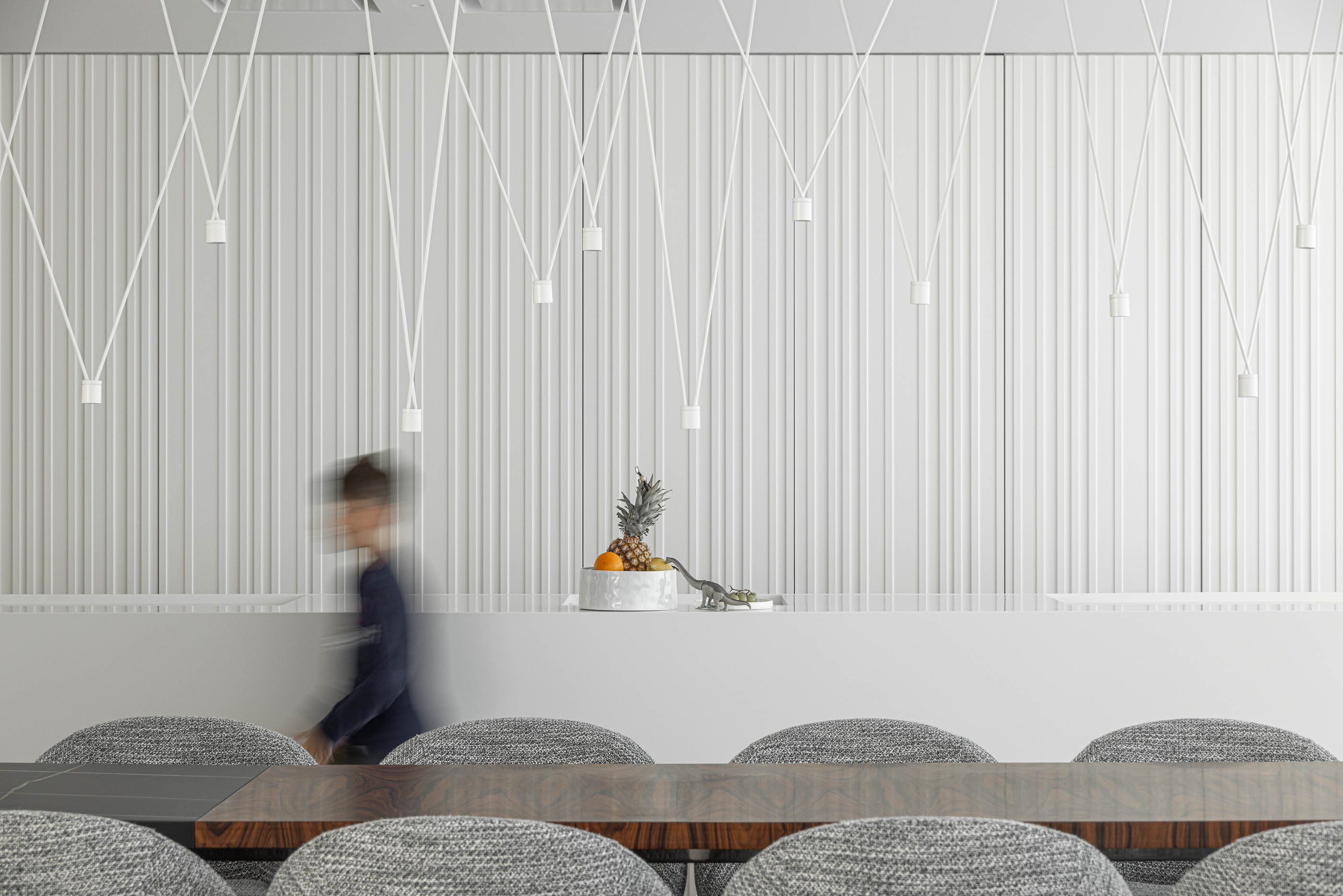 Cozinha: Ilha branca com tampo em madeira, cadeiras cinzentas e parede com revestimento vertical. — Riscowhite arquitetura Risco Singular em Barcelos