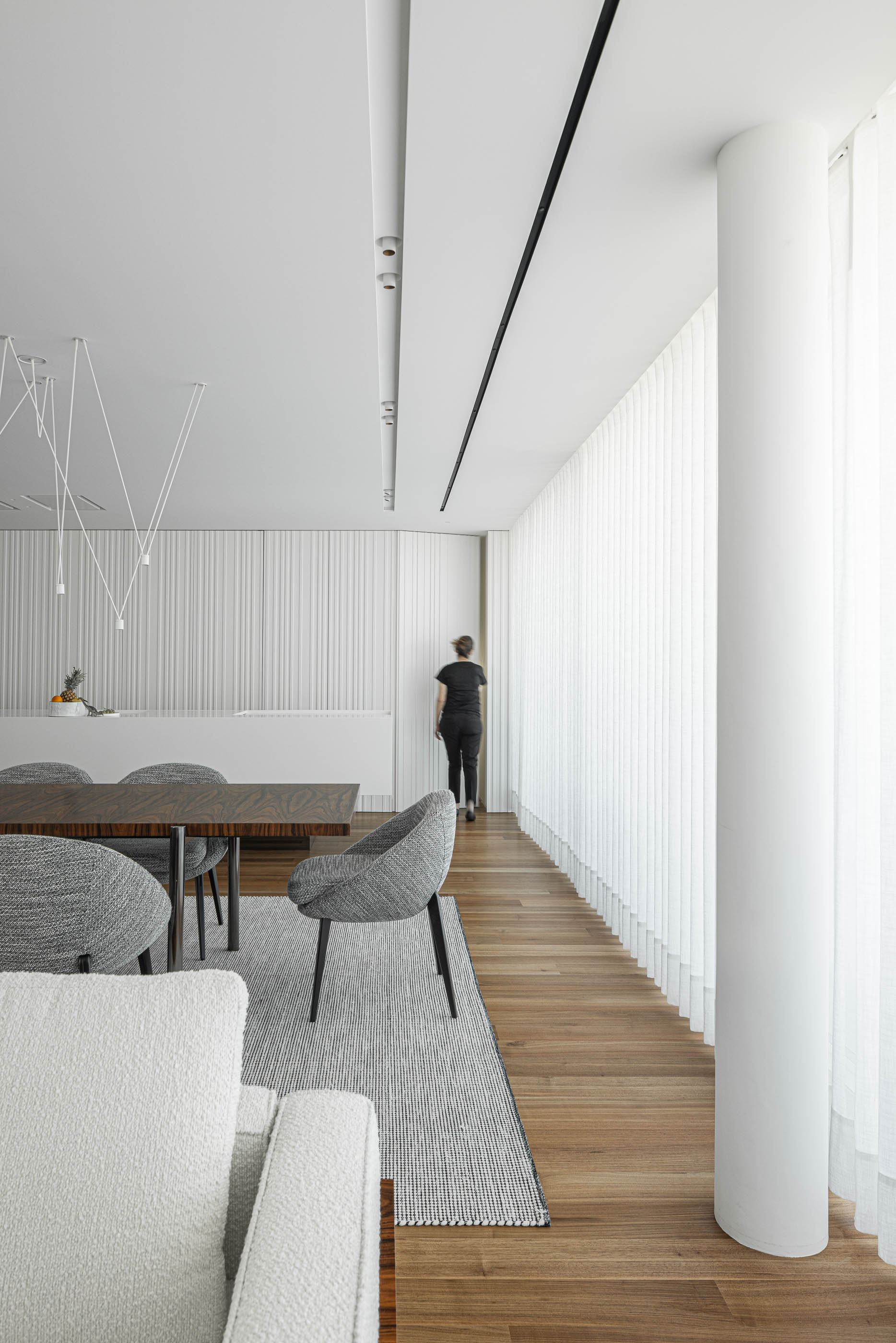 Sala de jantar: Detalhe da mesa de jantar, cadeiras cinzentas e parede com revestimento vertical branco. — Riscowhite arquitetura Risco Singular em Barcelos