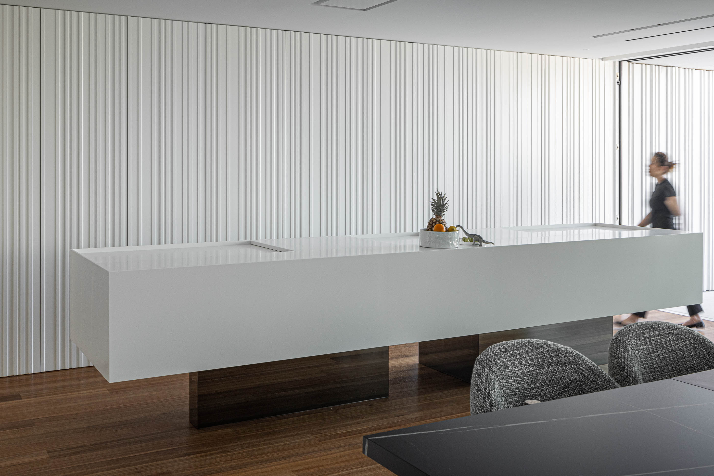 Cozinha: Ilha branca com base em madeira e cadeiras cinzentas em cozinha minimalista. — Riscowhite arquitetura Risco Singular em Barcelos