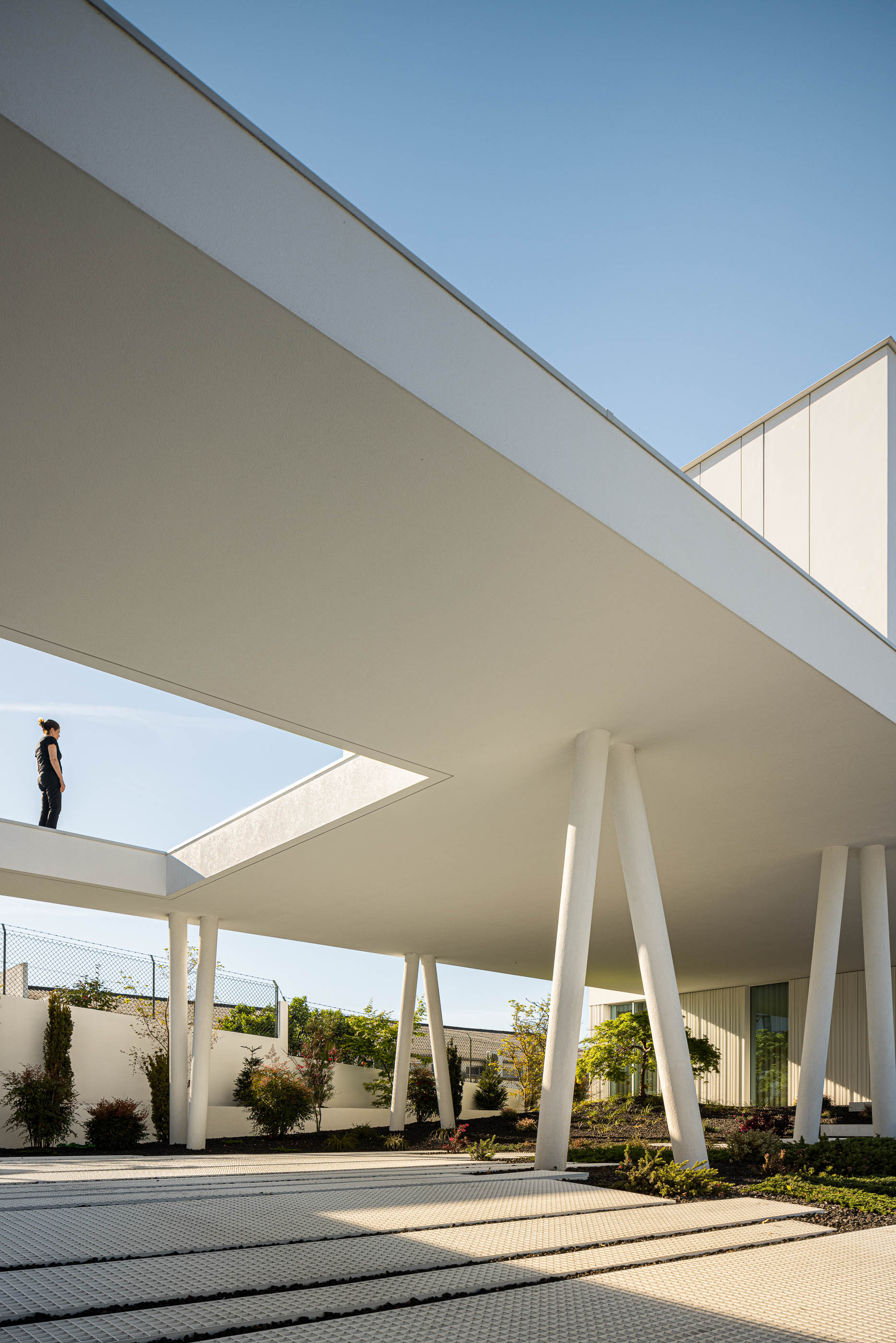 Exterior: Pátio com escada em caracol, jardim minimalista e passadiço elevado com pessoa. — Riscowhite arquitetura Risco Singular em Barcelos