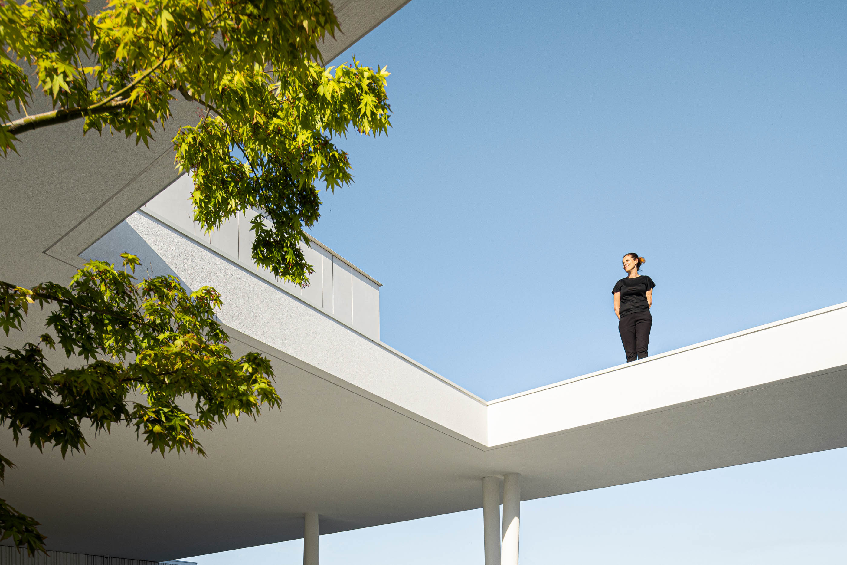 Exterior: Passadiço elevado com pessoa e vegetação, sob céu azul. — Riscowhite arquitetura Risco Singular em Barcelos