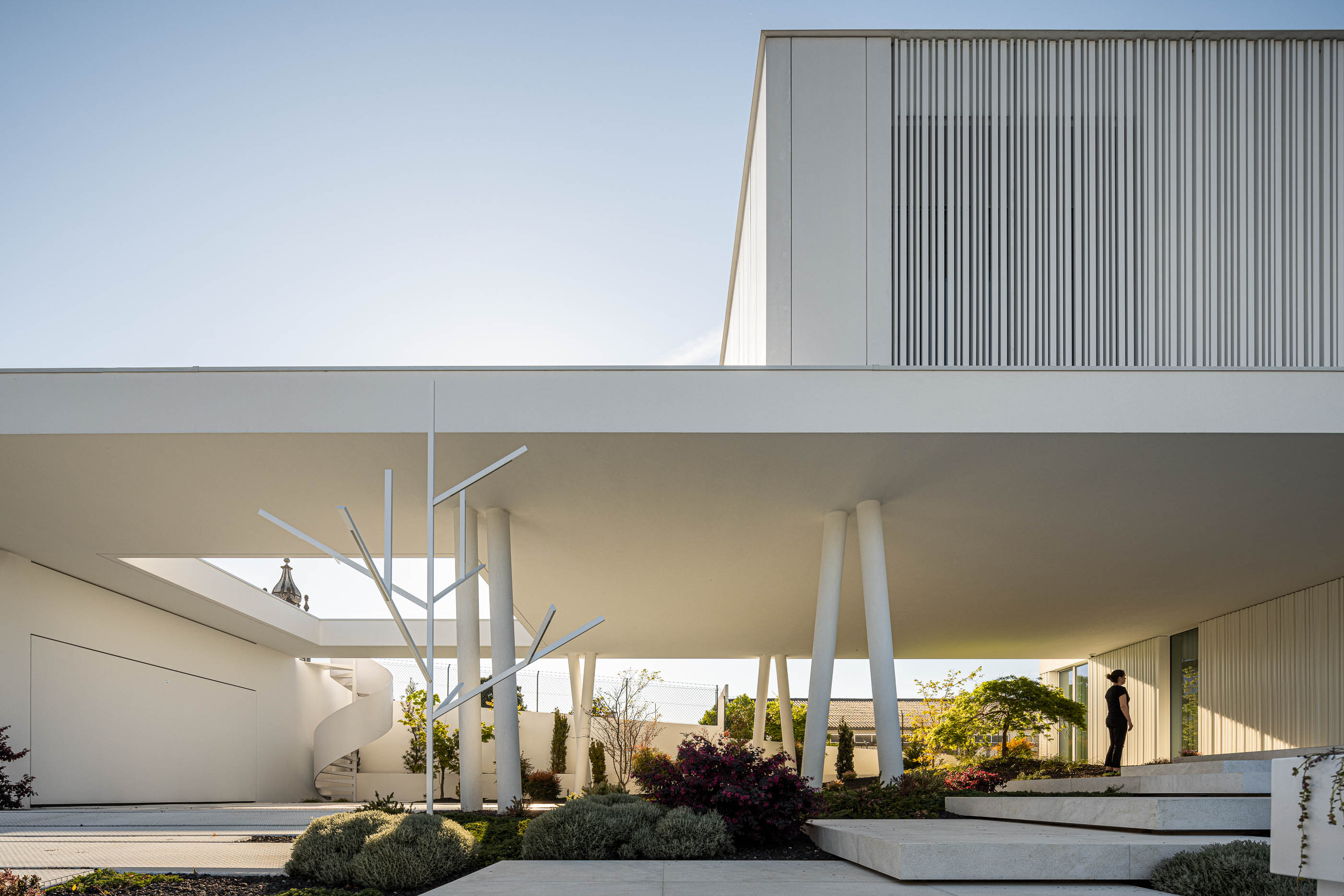 Exterior: Moradia branca com jardim minimalista, passadiço elevado e pessoa. — Riscowhite arquitetura Risco Singular em Barcelos