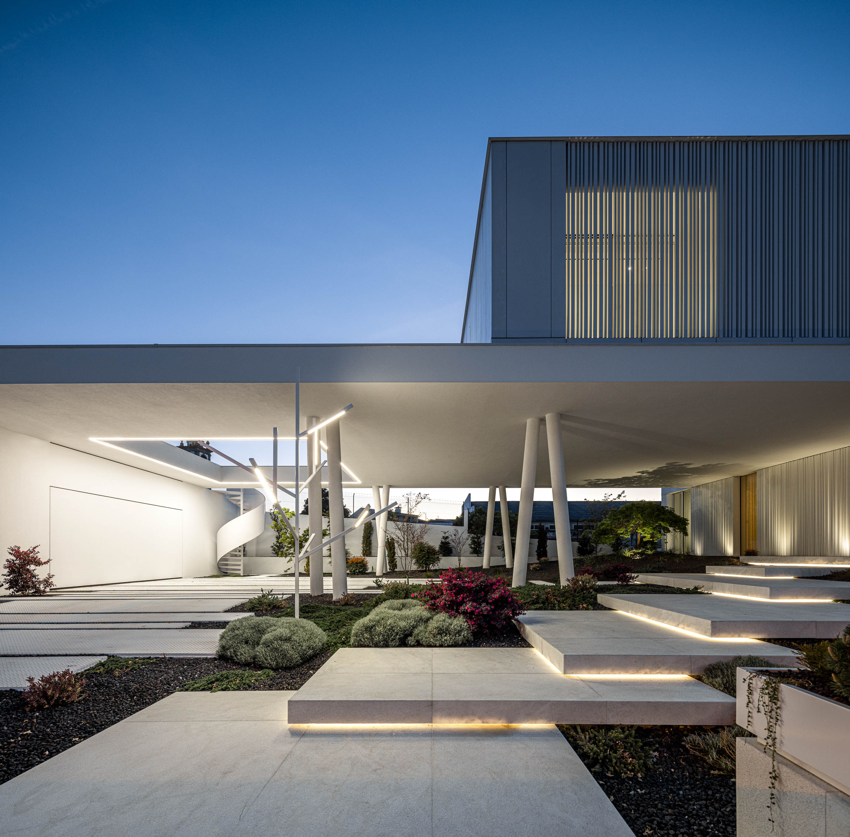 Exterior: Moradia branca iluminada à noite, com jardim minimalista e passagens em pedra iluminadas. — Riscowhite arquitetura Risco Singular em Barcelos
