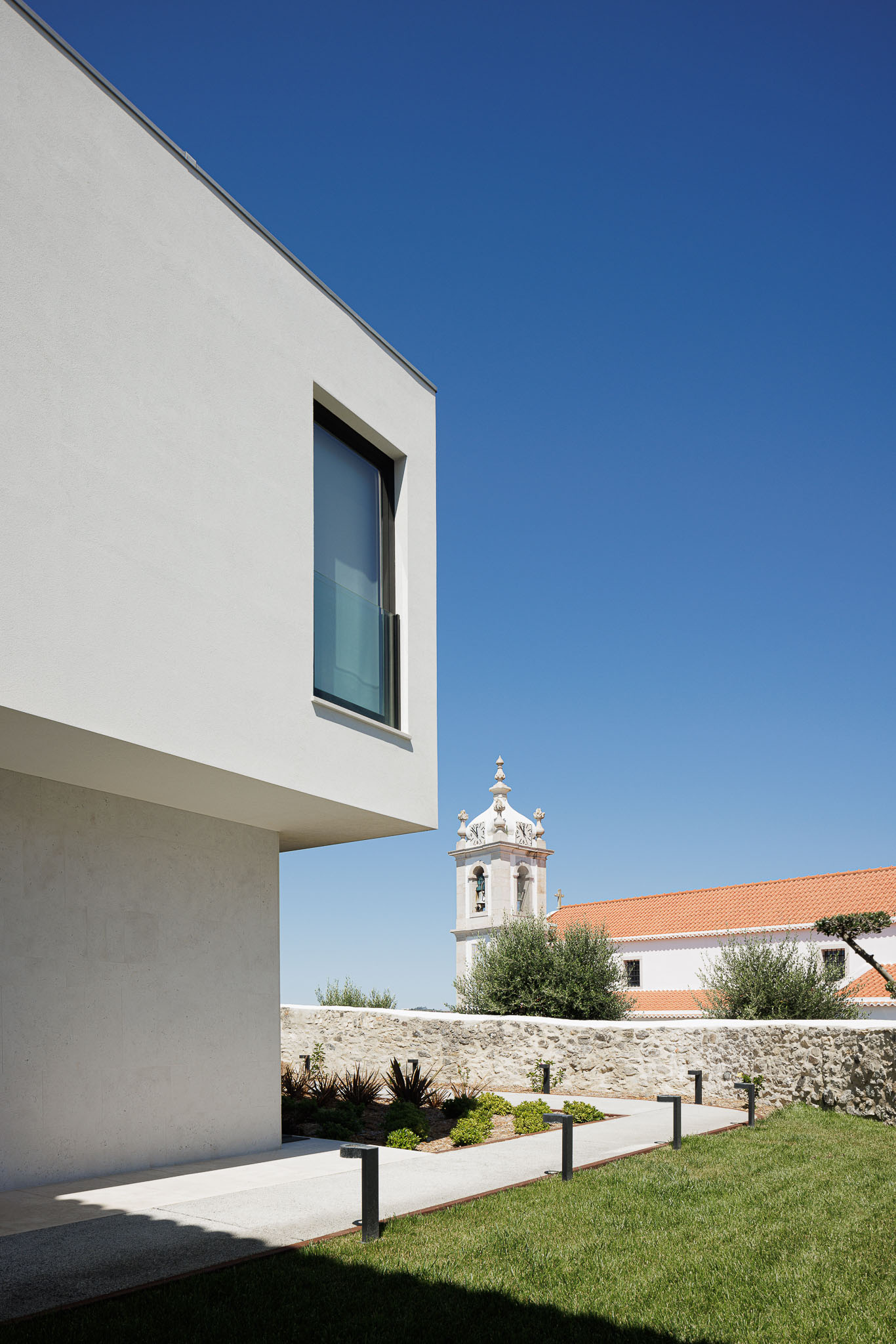 Exterior: Edifício moderno com linhas retas, jardim relvado e vista para a torre da igreja. — Farmácia NR arquitetura Esquissos Arquitectura em Sintra