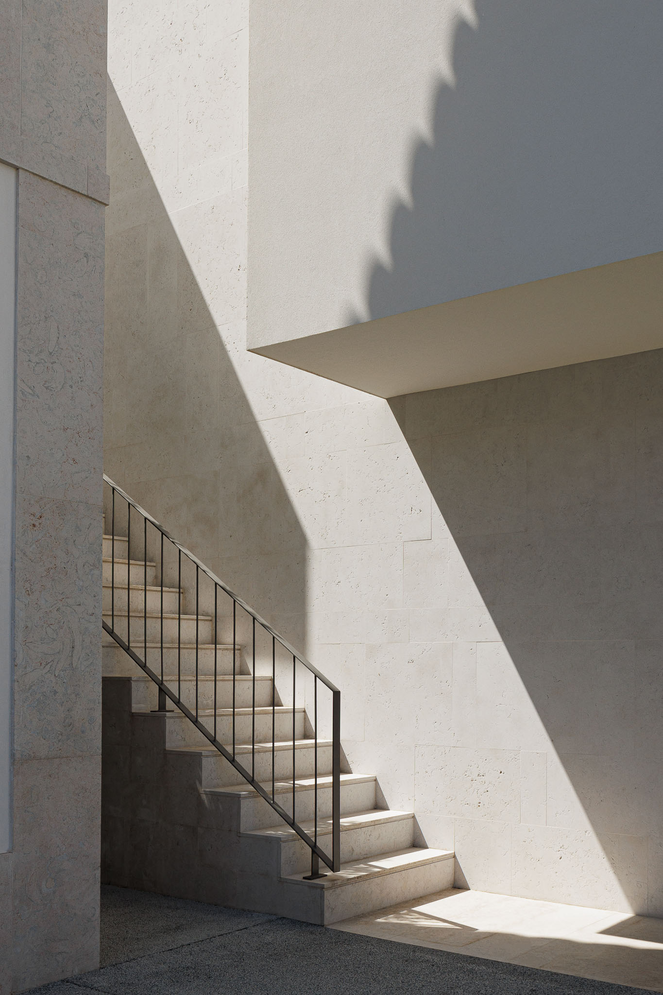 Exterior: Escadas exteriores em pedra clara com corrimão metálico, paredes revestidas a pedra. — Farmácia NR arquitetura Esquissos Arquitectura em Sintra