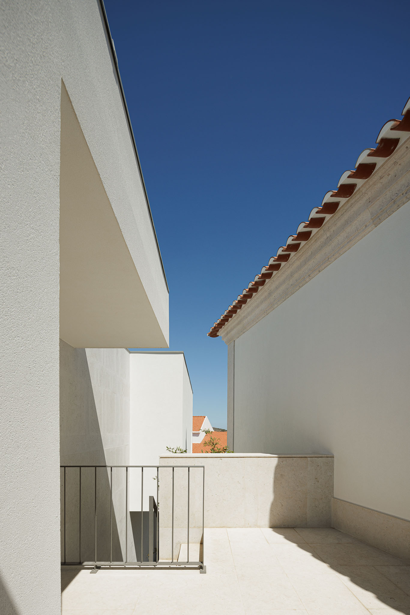 Exterior: Pátio com pavimento em pedra, paredes brancas e vista para o céu e telhado cerâmico. — Farmácia NR arquitetura Esquissos Arquitectura em Sintra
