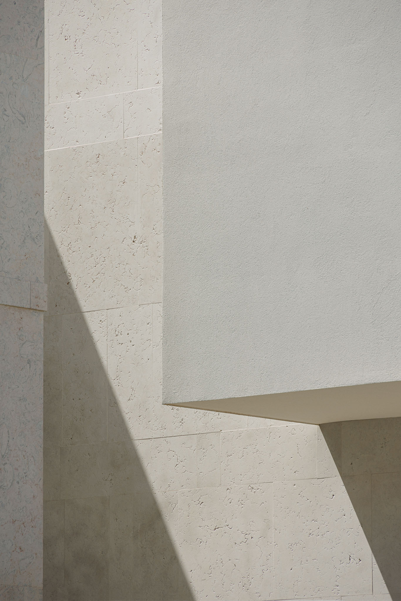 Exterior: Detalhe da arquitetura com volumes geométricos, revestimentos em pedra e reboco branco. — Farmácia NR arquitetura Esquissos Arquitectura em Sintra